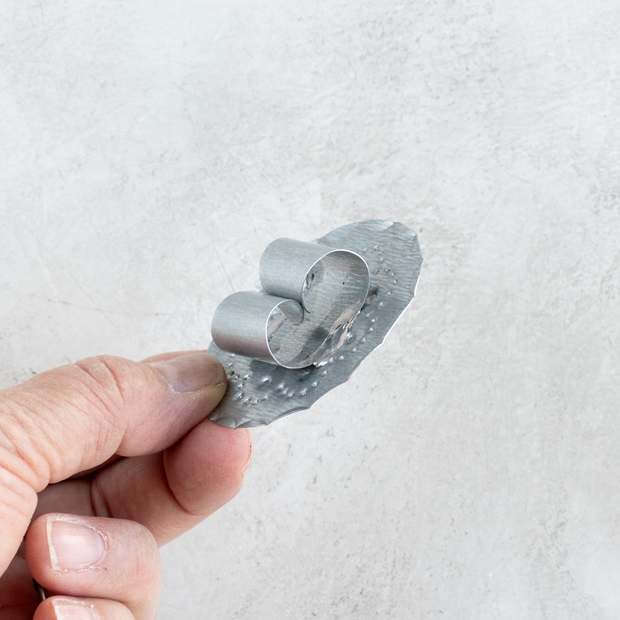 Back view of the Roseta bandana slide, showing the hand-formed metal loop attachment held in hand for scale.