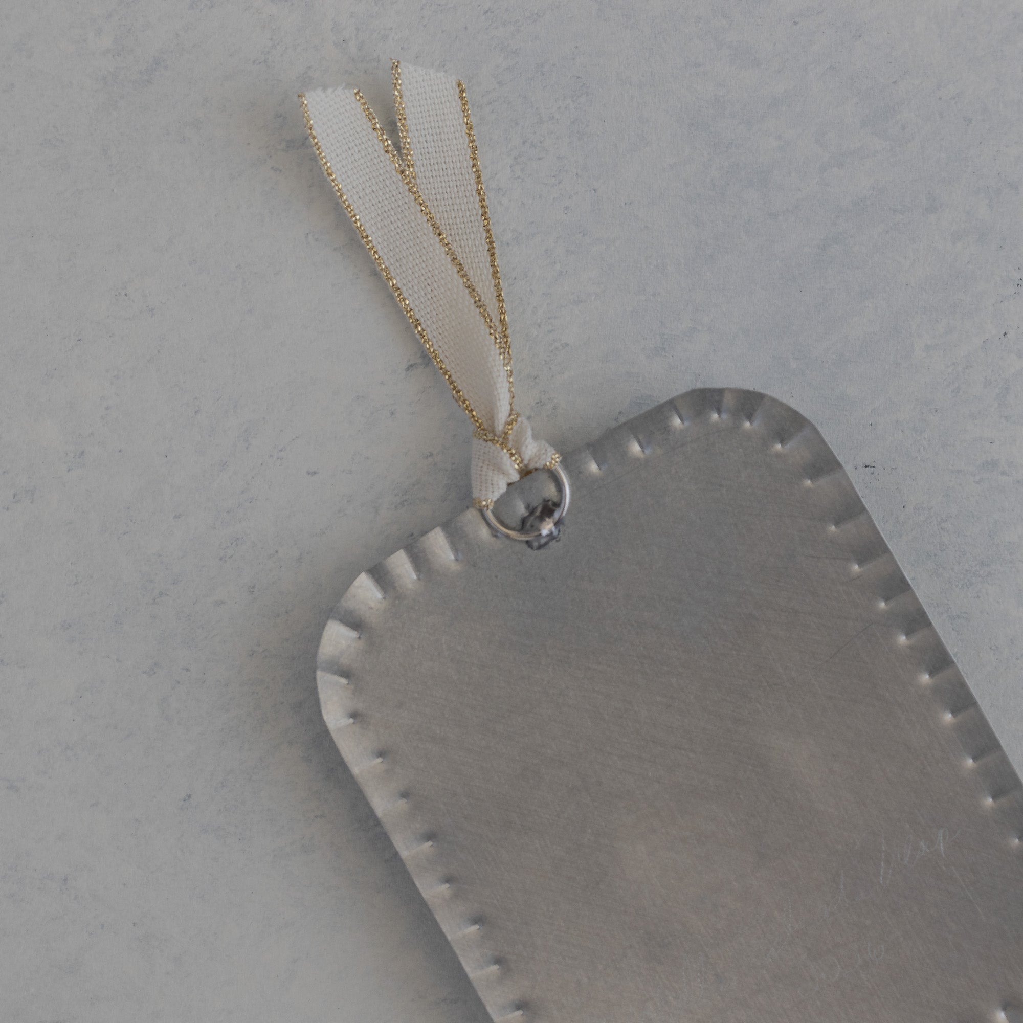 Back of the Sacred Heart Milagro, Dimensional, showing scalloped edge and ivory ribbon with gold accent