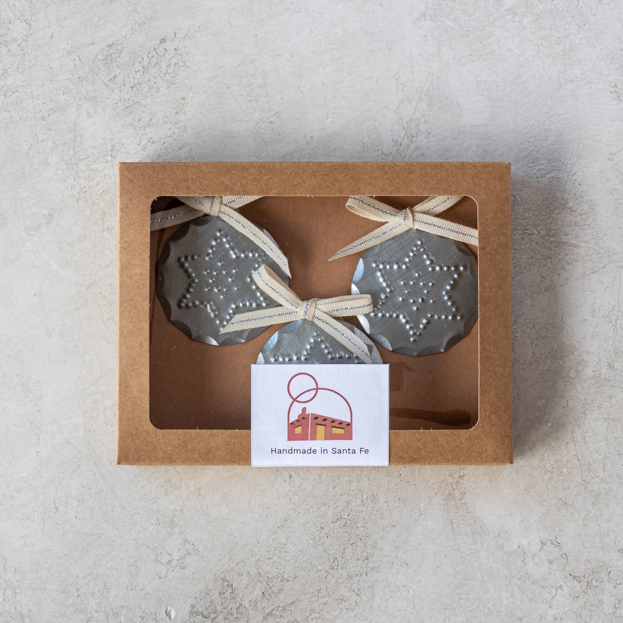 Gift-ready set of three 2” tin Luz Estrella Mini Ornaments in kraft window box with Studio Carta ribbon.