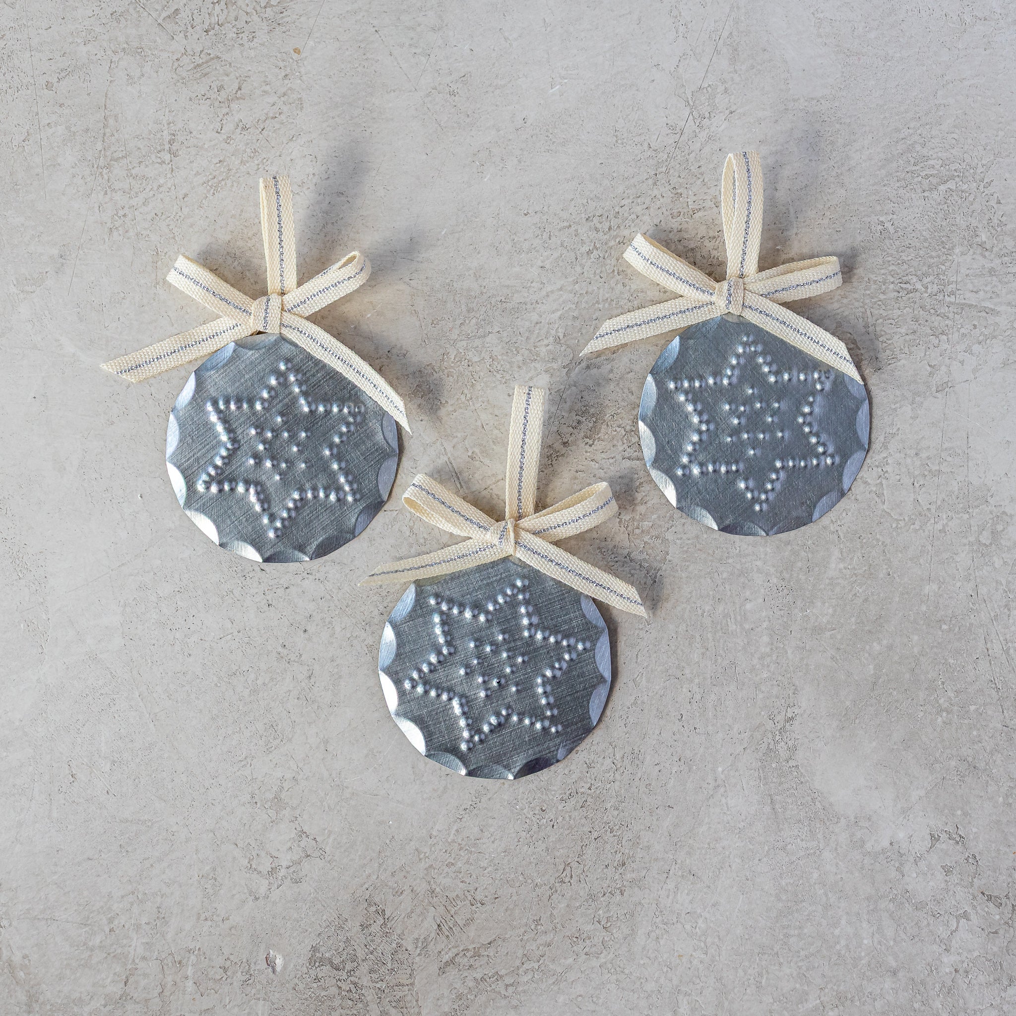 Set of three 2” tin Luz Estrella Mini Ornaments with Studio Carta ribbon, shown loose on neutral background.