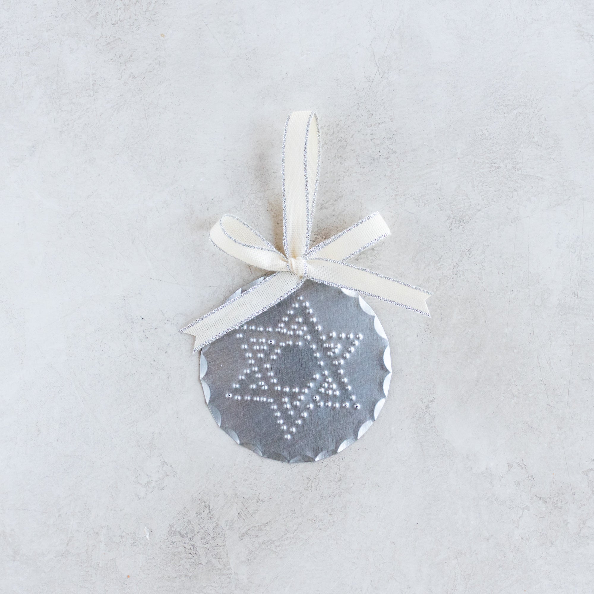 3-inch handmade tin ornament with punched Star of David design, scalloped edge, and Studio Carta cotton ribbon with metallic trim.