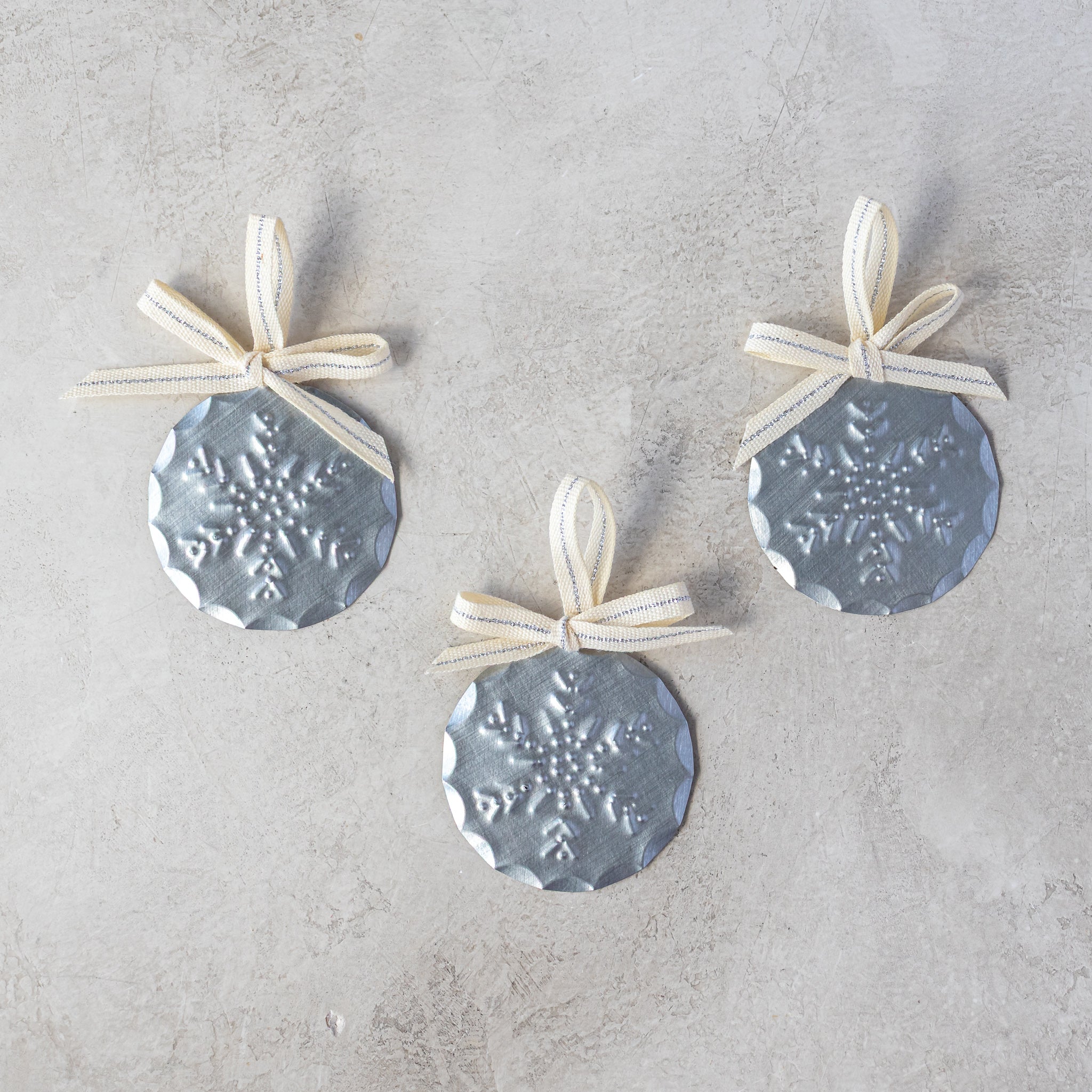 Set of three 2” tin Luz Nieve Mini Ornaments with Studio Carta ribbon, shown loose on neutral background