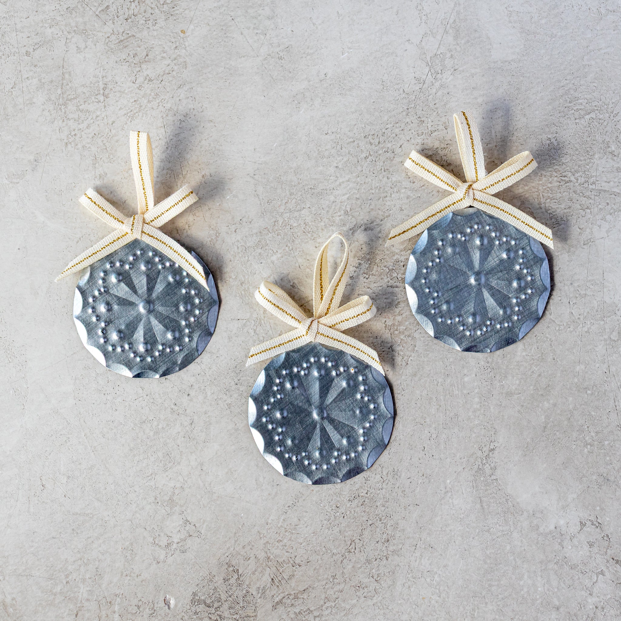 Set of three 2” tin Luz Roseta Mini Ornaments with Studio Carta ribbon, shown loose on neutral background.