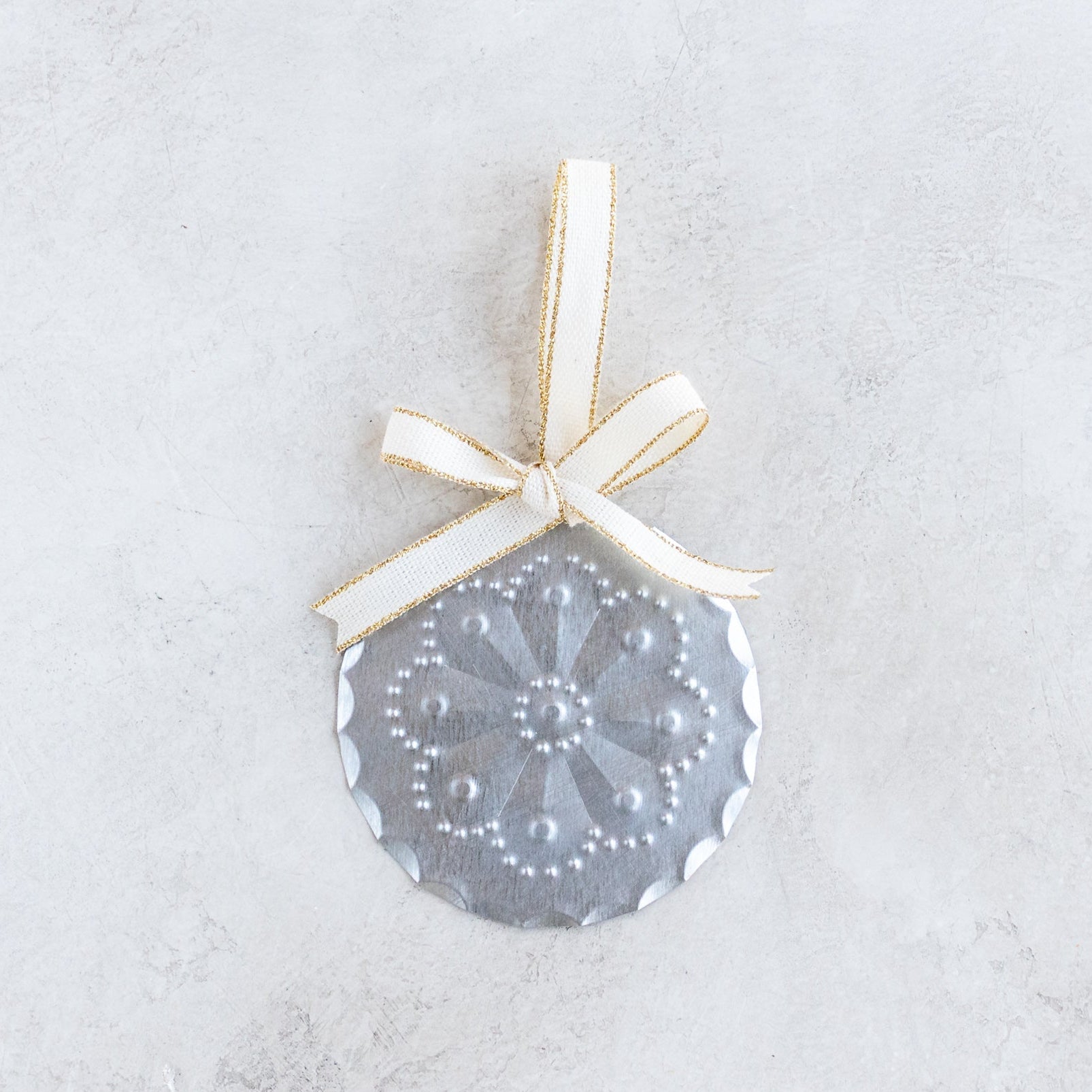 3-inch handmade tin ornament with punched rosette floral design, scalloped edge, and Studio Carta cotton ribbon with metallic gold accent.
