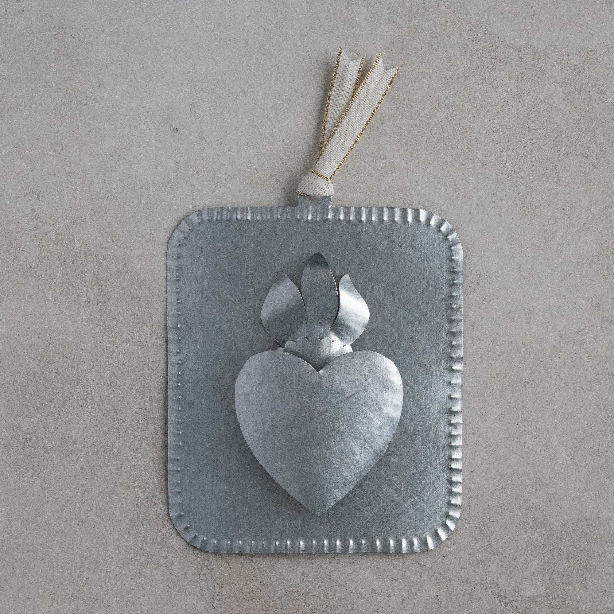 Handmade tin ornament featuring a raised flaming heart design on a square, scalloped-edge tin plate, photographed against a light textured background.