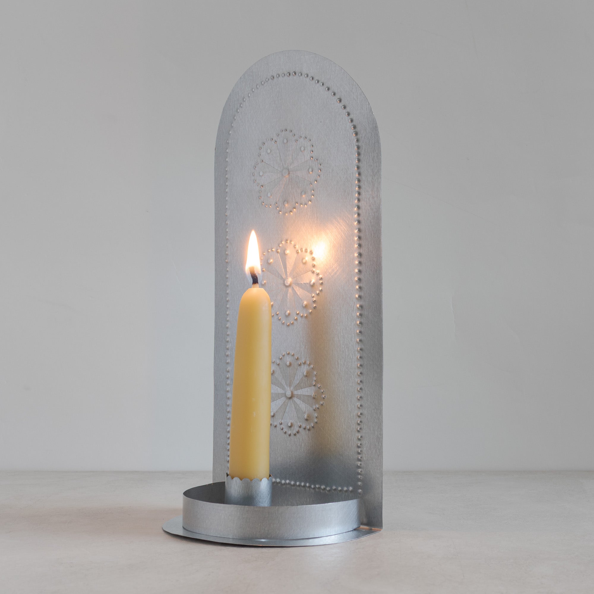 Decorative metal candle holder with a lit yellow candle on a plain background