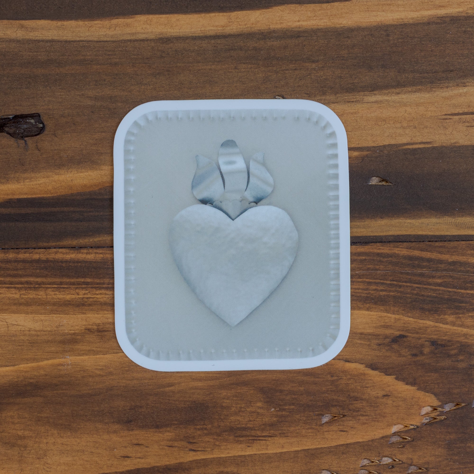 Sacred Heart sticker close up on dark wood grain, showing raised heart and bow relief detail and crimped border