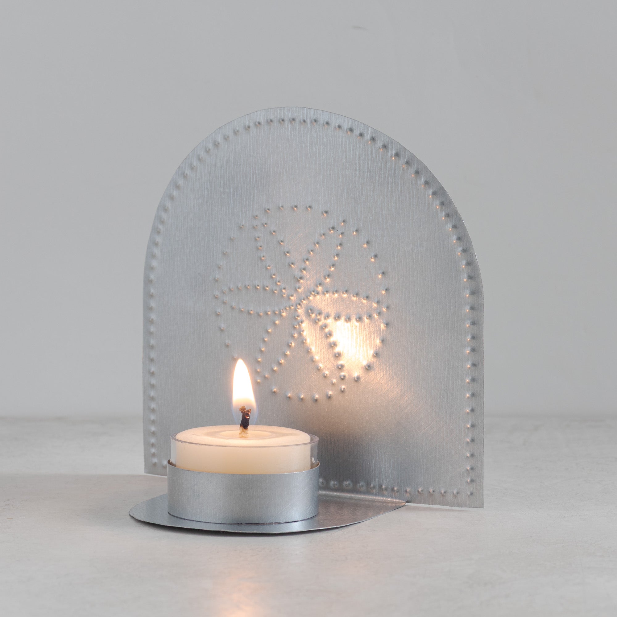 Flor tealight candleholder in natural tin glowing with lit beeswax candle