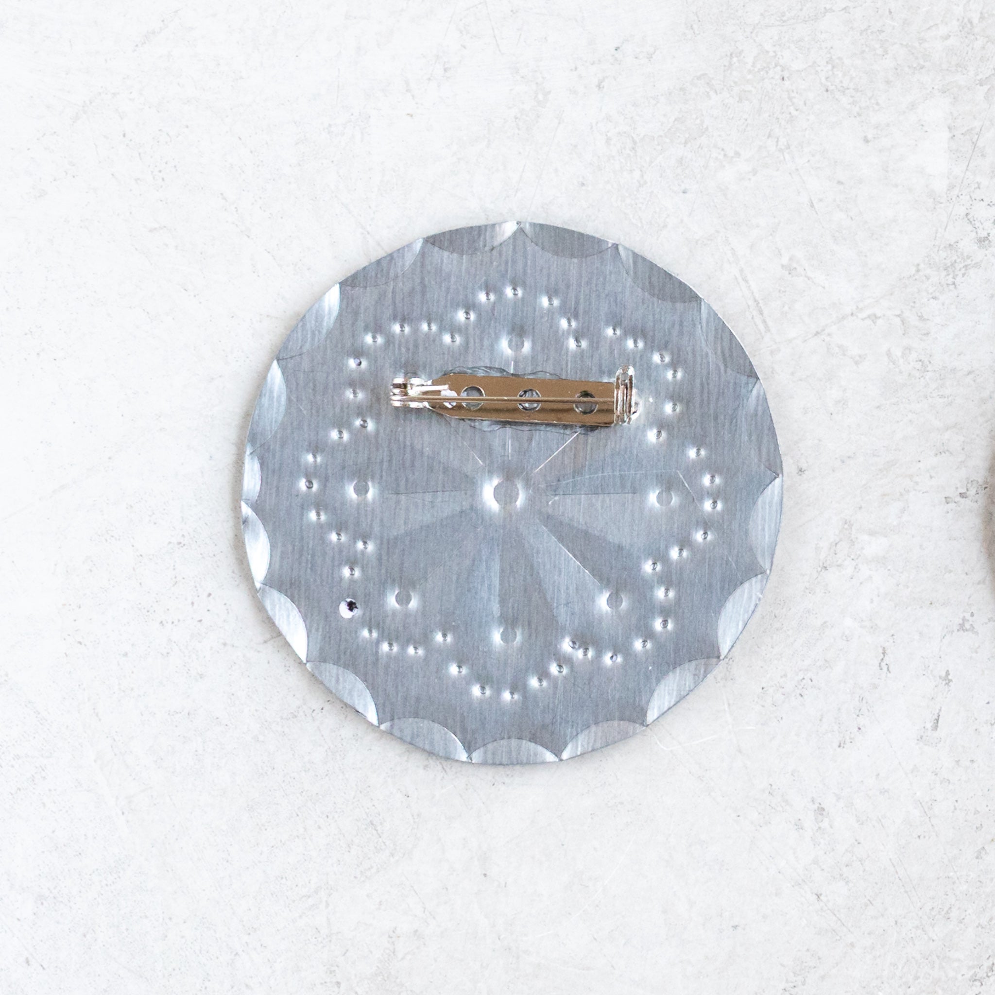Front view of the Accent Roseta Pin with 2-inch hand-stamped rosette design in tin.