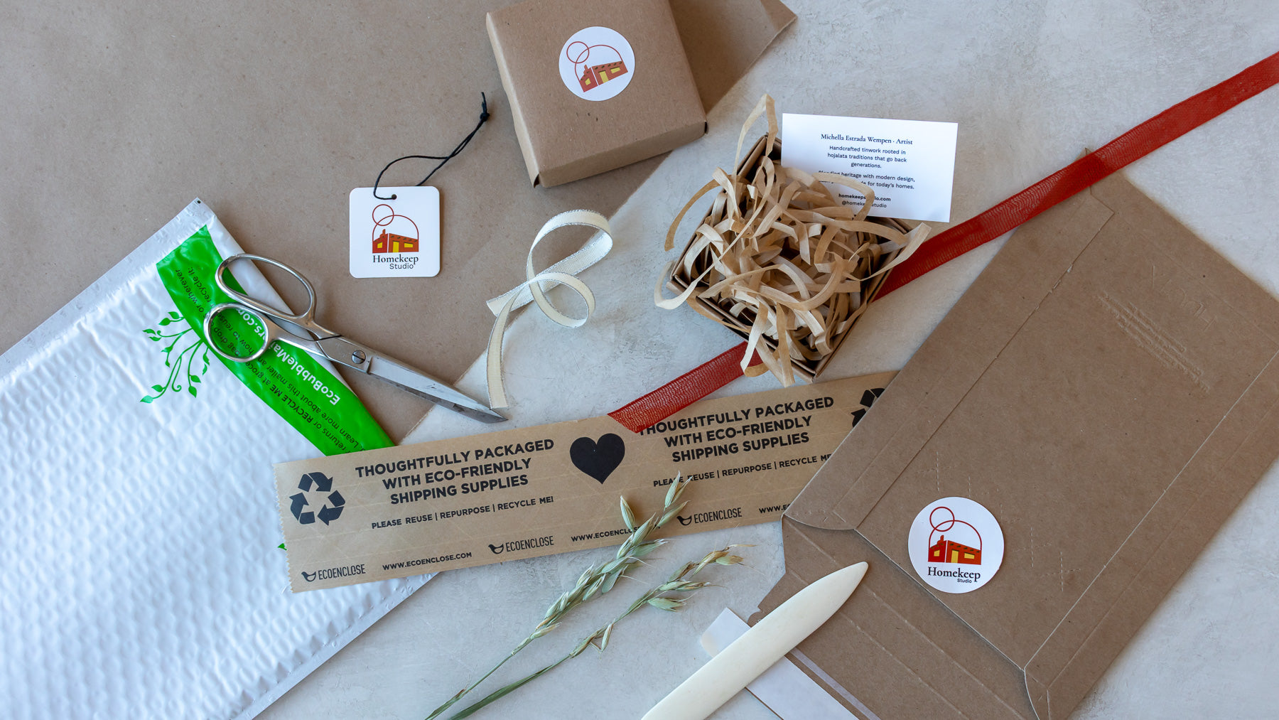 Flat lay of eco-friendly packaging supplies from Homekeep Studio, including kraft boxes, water-activated tape, spiro pack fill, recyclable mailers, and branded stickers arranged on kraft paper.
