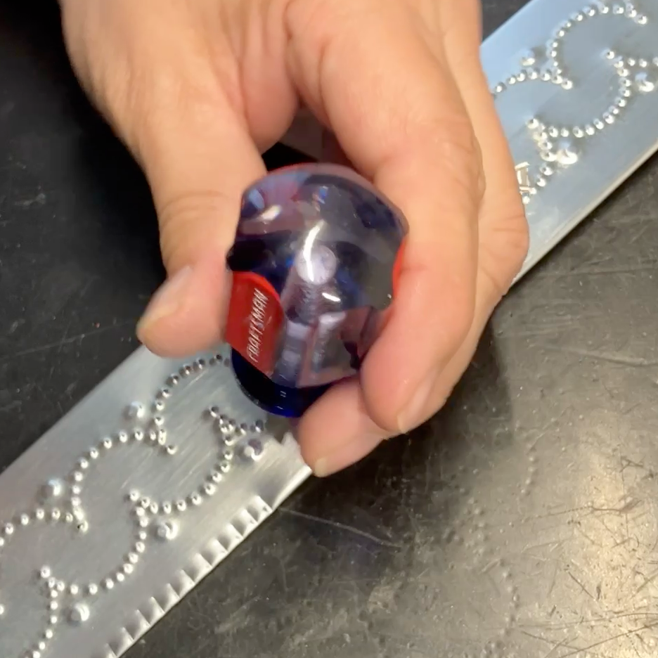 Hand punching a repeating pattern into metal tinwork by hand