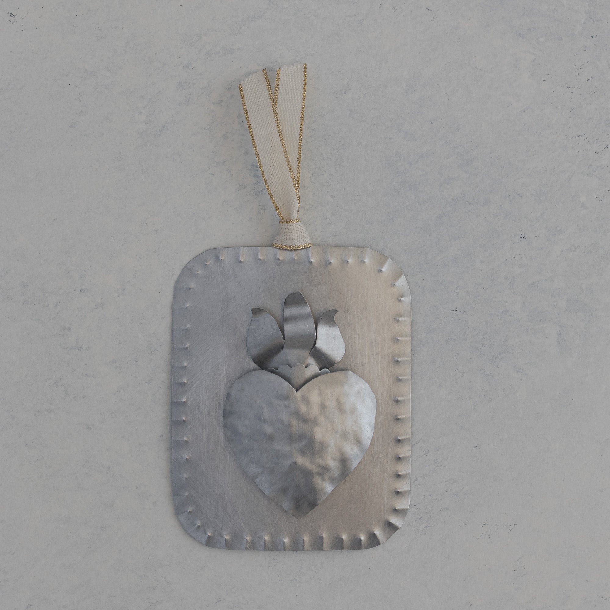 Hand formed tin sacred heart milagro with raised dimensional heart and flame, scalloped edge and ivory ribbon with gold accent