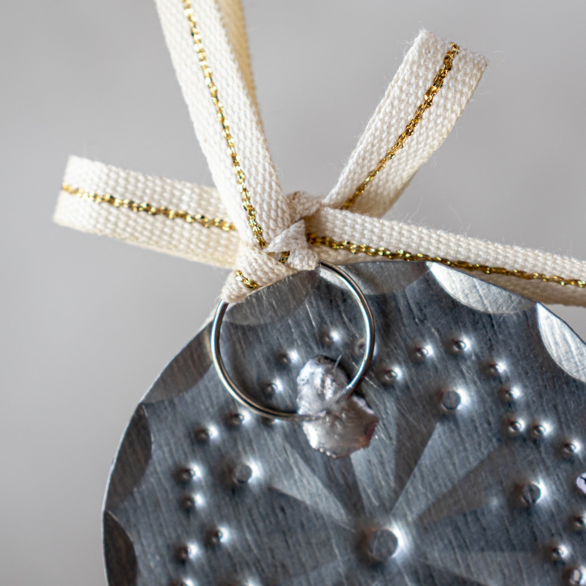Close-up of back of 2” tin mini ornament showing soldered ring attachment and Studio Carta ribbon.