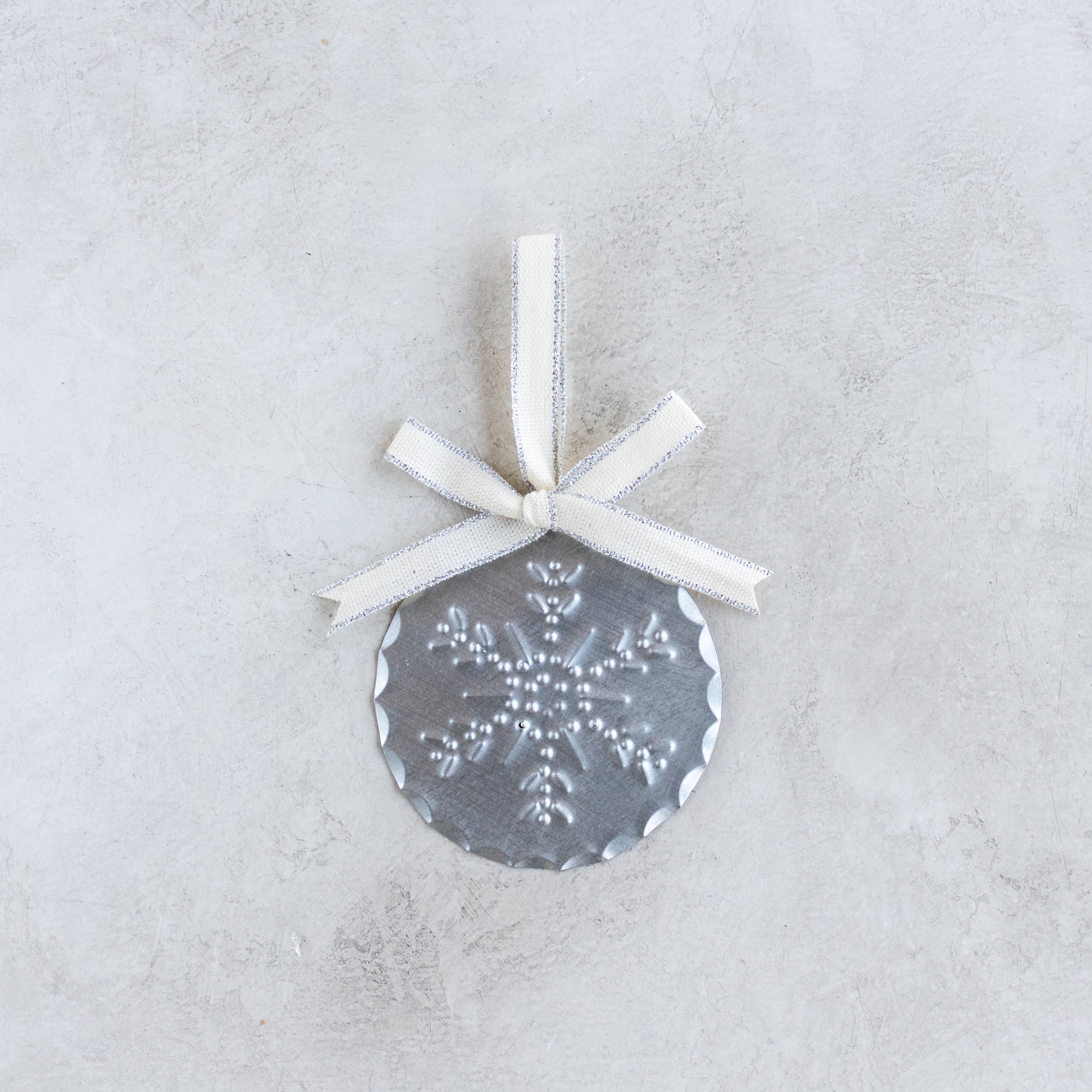 3-inch handmade tin ornament with punched snowflake design, scalloped edge, and Studio Carta cotton ribbon with metallic accent.