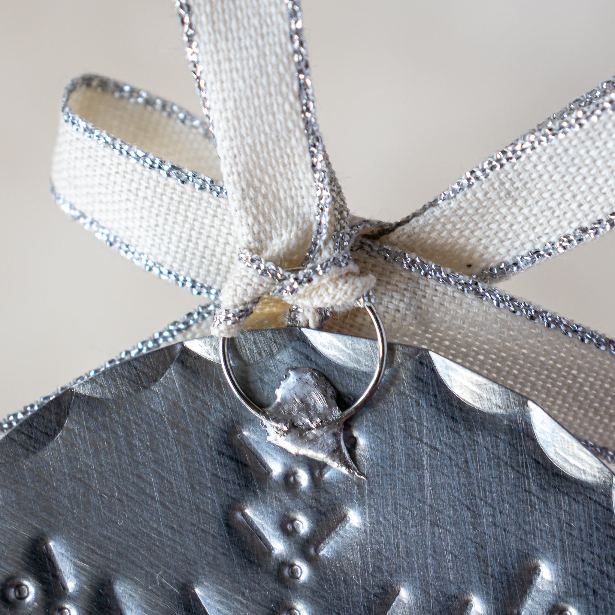 Close-up of back of 3” tin ornament showing soldered ring attachment and Studio Carta ribbon.