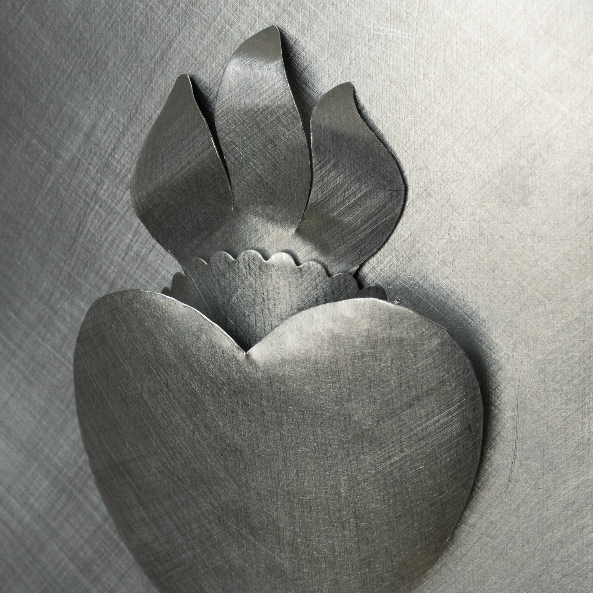 Detailed close-up of a raised tin Sacred Heart ornament, showing the layered metalwork and brushed texture