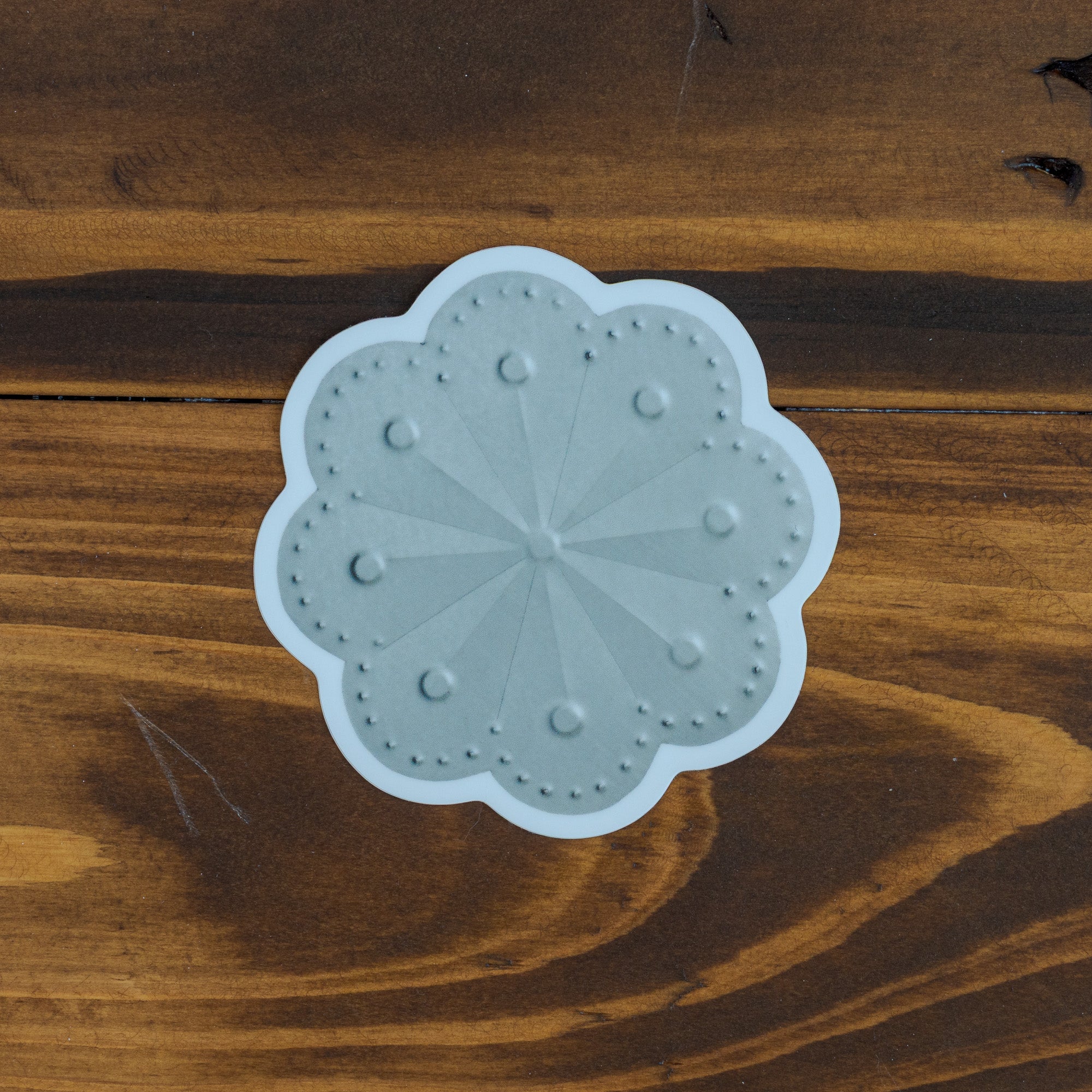 Roseta sticker close up on dark wood grain, showing punched petal pattern and scalloped edge