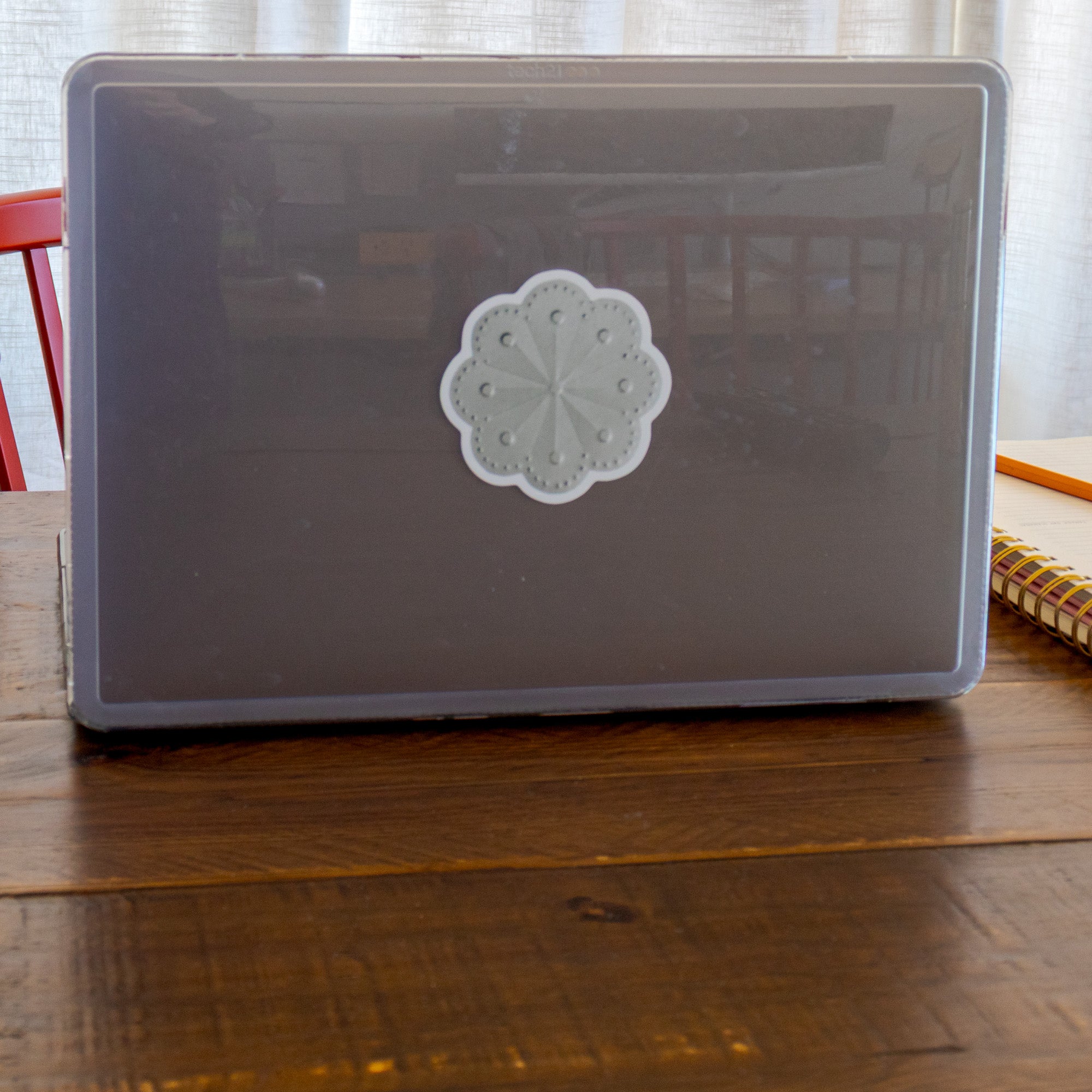 Roseta sticker on a grey laptop case on a dark wood table, red chair and linen curtains in background