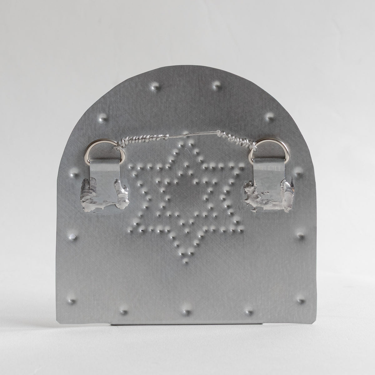 Back of a punched Star of David tinwork candleholder with two loops and a wire hanger attached.