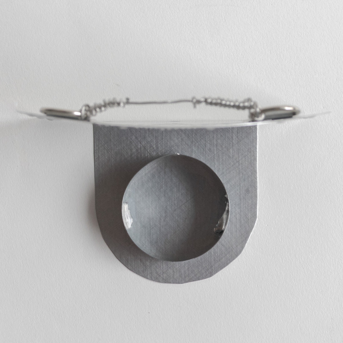 Top view of a silver metal candle holder showing the cup for the tealight and the hanging wire on the back. 