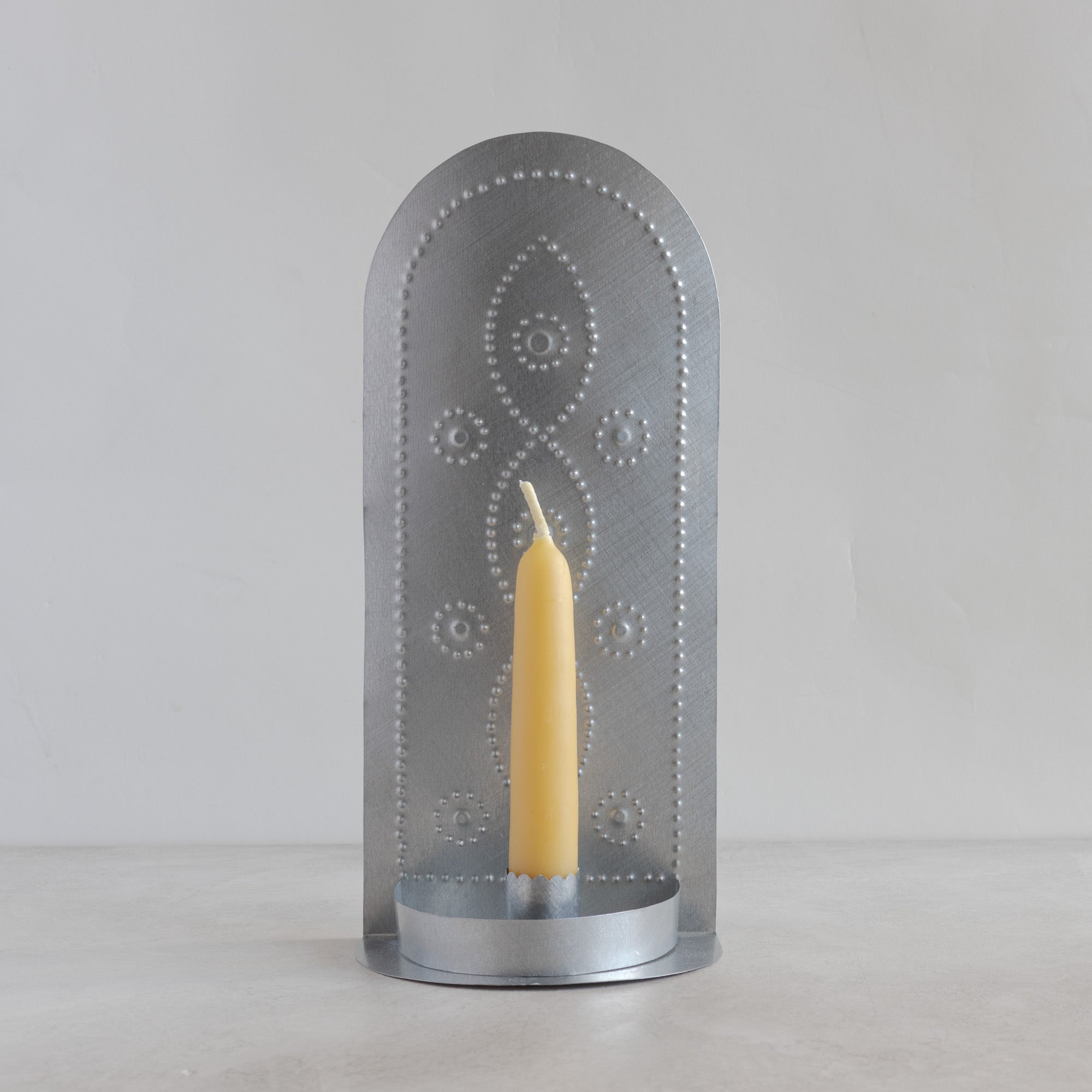 Hand-punched tin taper candleholder with vine motif and beeswax taper candle, front view on light background