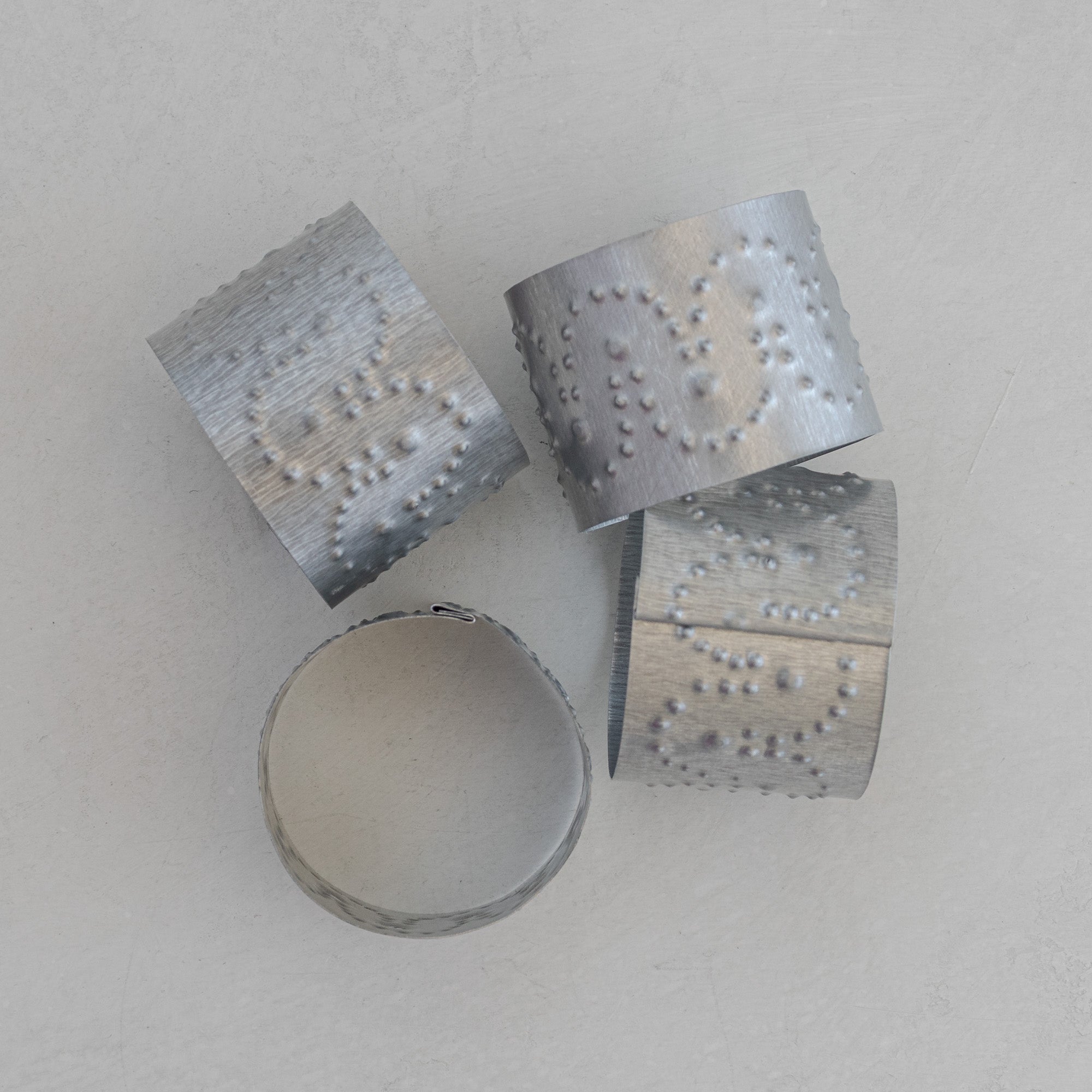 Single Arco tin napkin ring held by hand showing interior surface, hand-punched dot pattern visible through the tin, and folded seam construction detail.