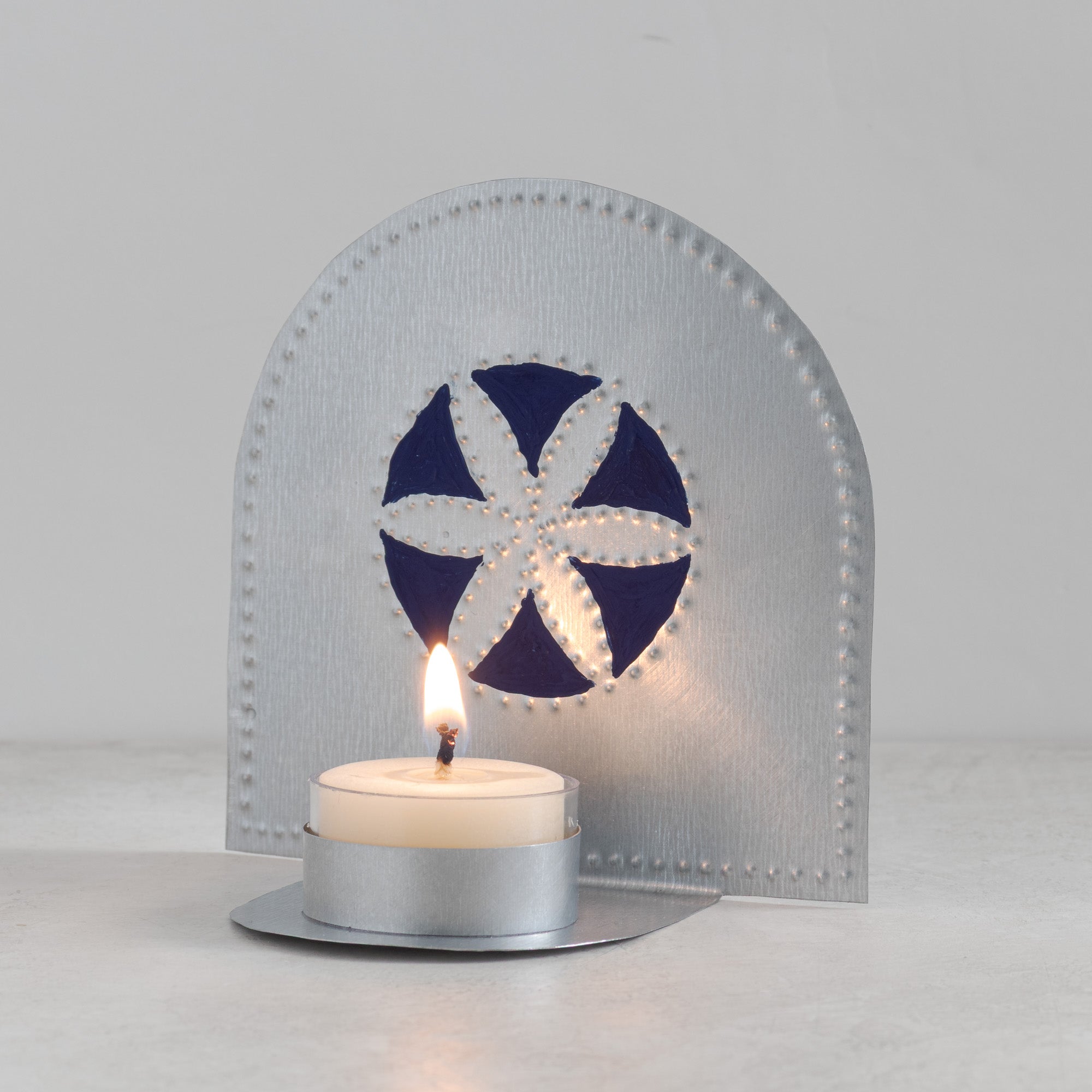 Flor tealight candleholder with hand-painted blue design glowing with lit candle