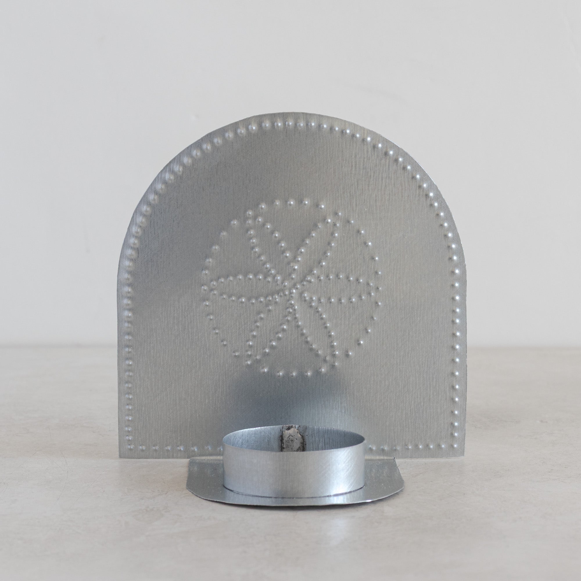 Hand-punched tin tealight candleholder with rosette motif in natural tin finish on light background