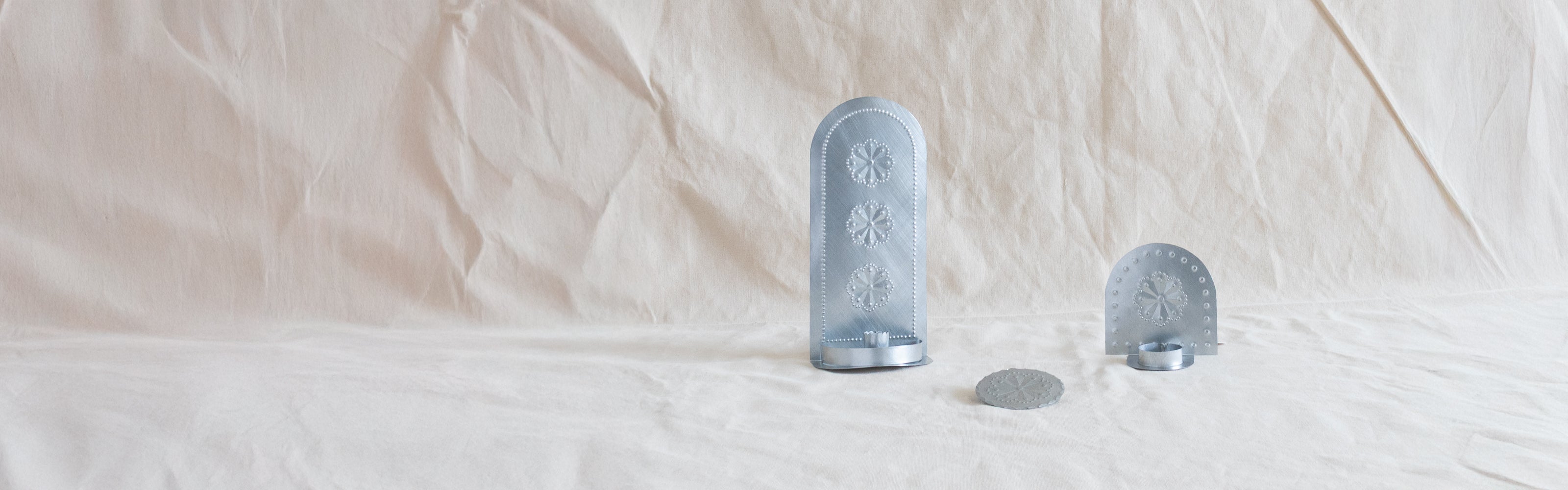 Handcrafted tin candleholders on a soft fabric backdrop.