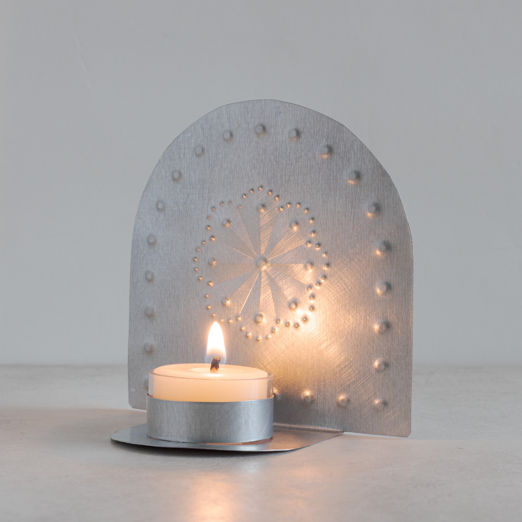 Luz Roseta handmade tin tealight candleholder glowing with lit beeswax tealight