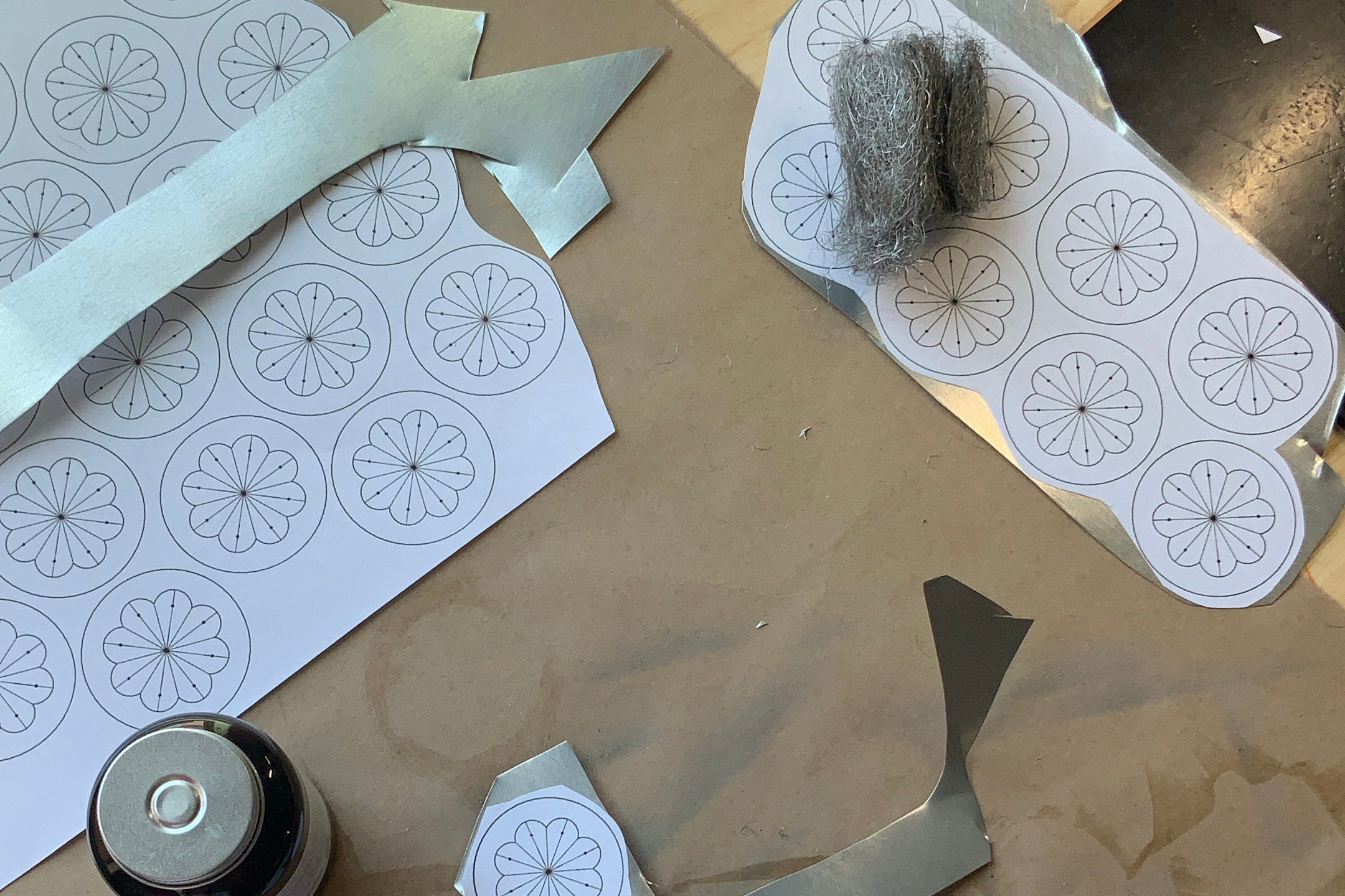 Tin sheet with cut patterns, paper templates, and steel wool on a worktable — showing materials used in Homekeep Studio tinwork.