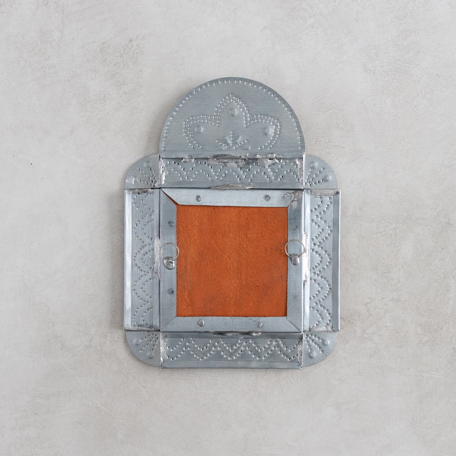 Decorative tinwork frame with tile back showing the hanger on a light gray background