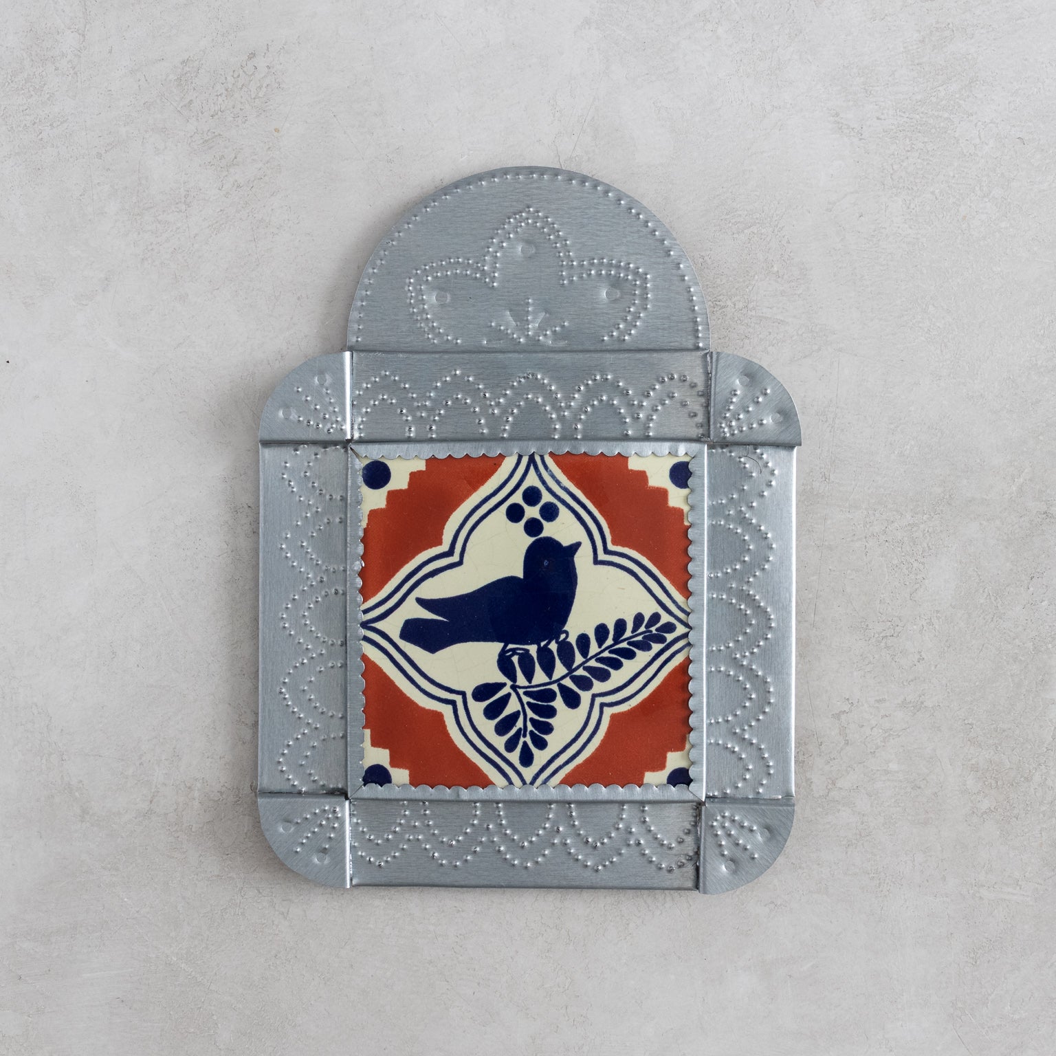 Decorative tinwork framed wall tile with a blue bird design on an orange and cream background, set against a light gray background.