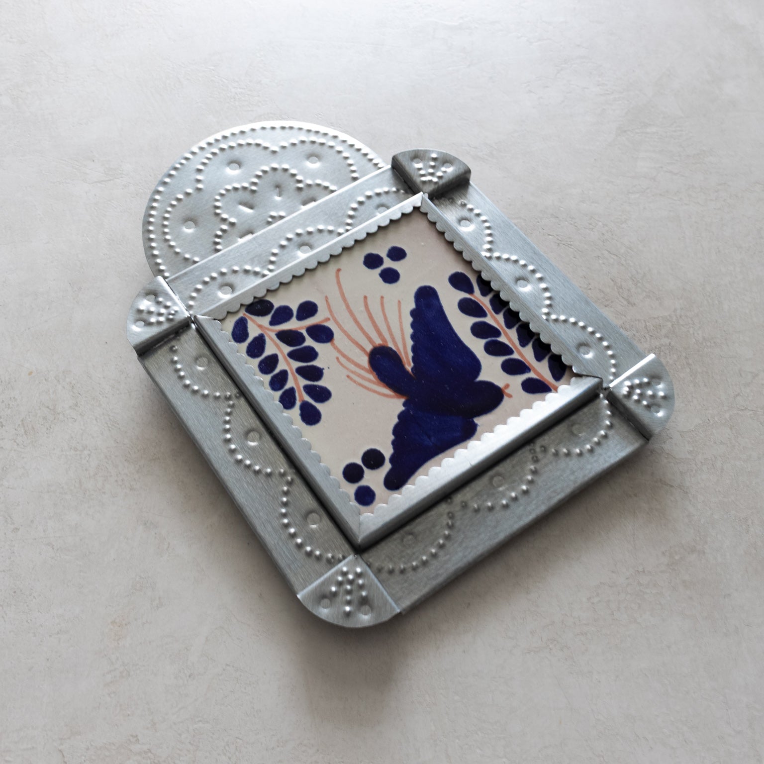 Decorative tinwork framed tile with blue bird design on a light gray background