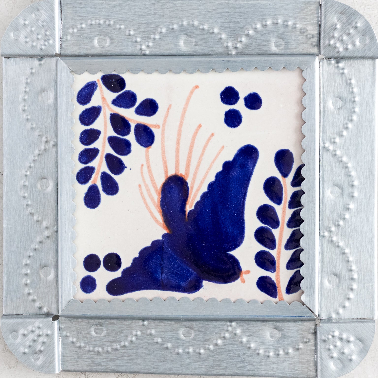 Closeup of a decorative tinwork framed tile with a blue bird design on a white background.