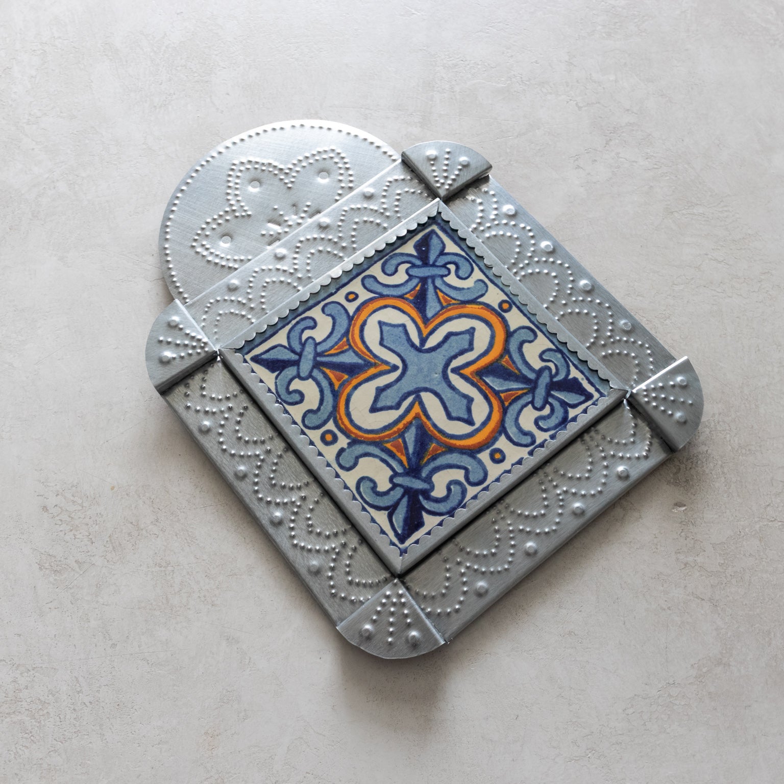 Decorative tinwork framed tile with geometric pattern on a light gray background