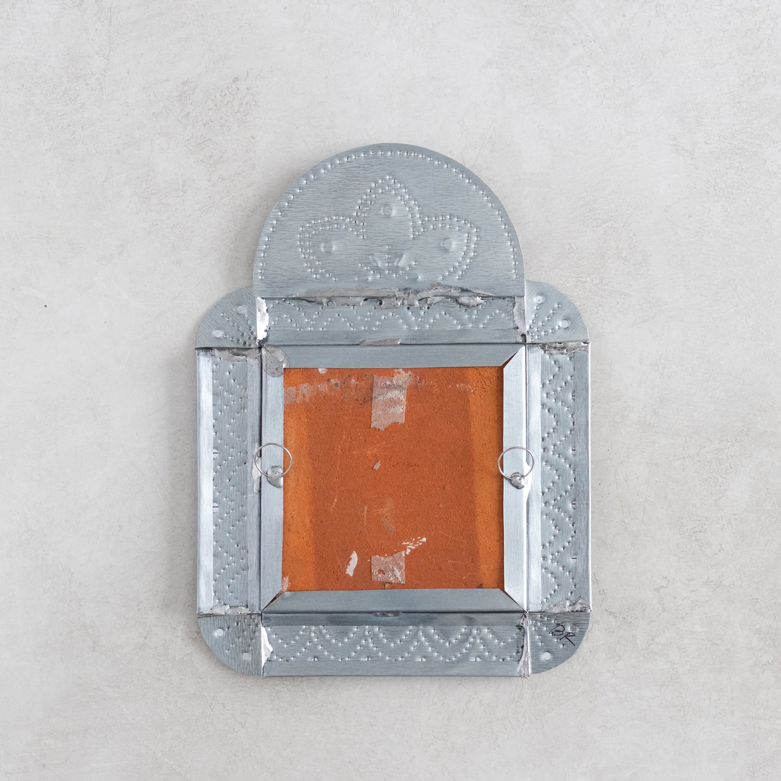 Decorative tinwork framed tile back showing hangers on a light gray background