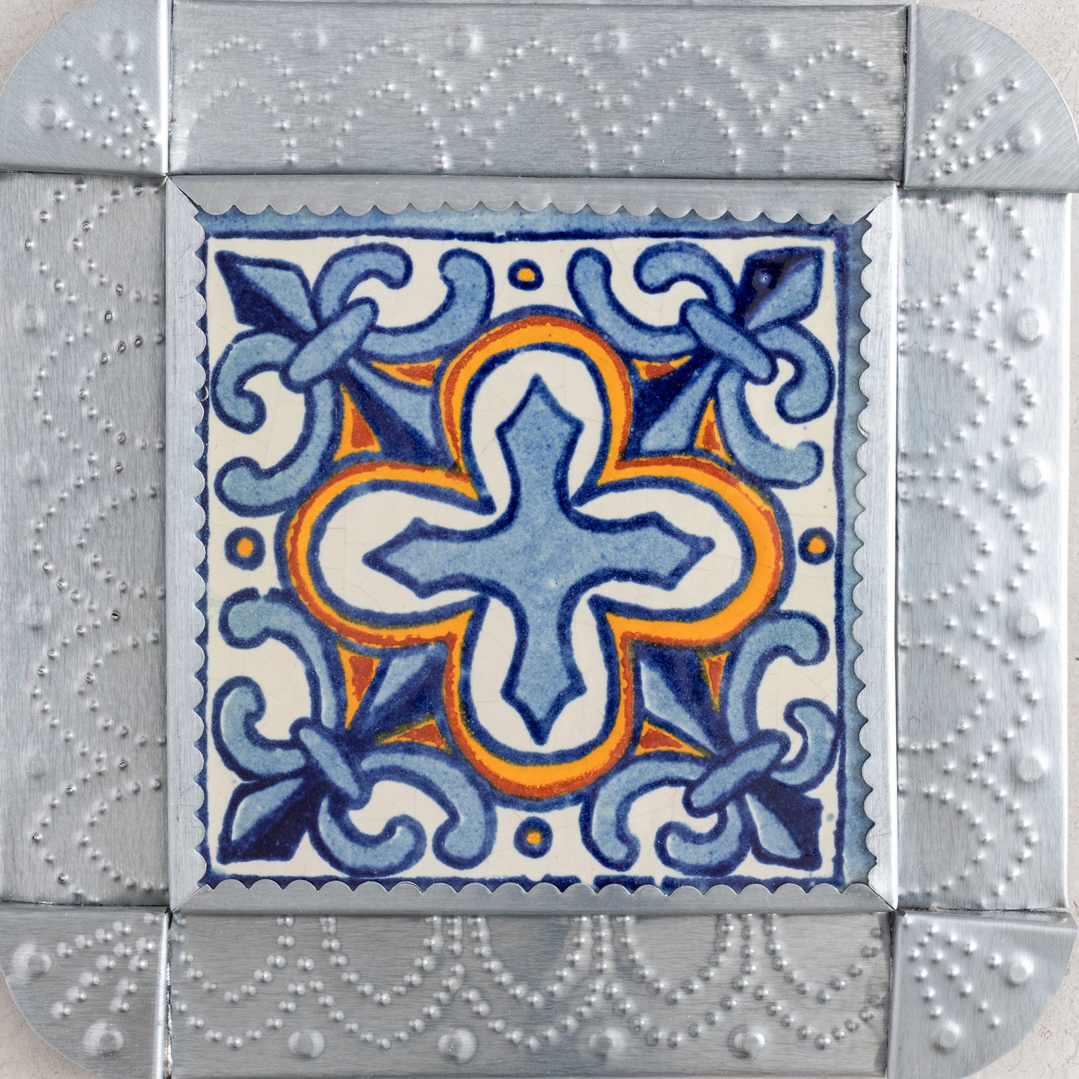 Closeup of a decorative tinwork framed tile with blue and orange design 