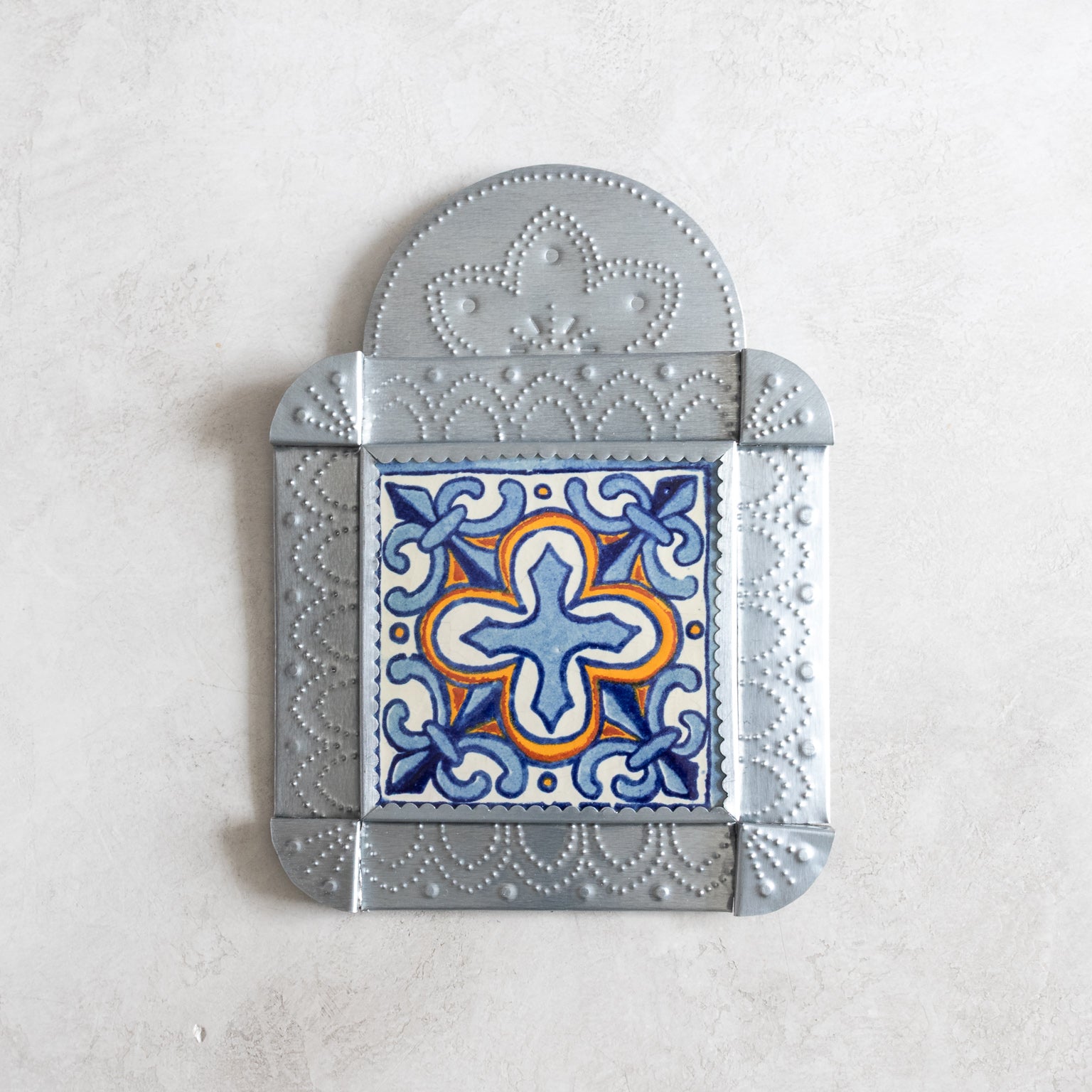 Decorative tinwork framed tile with floral design on a light gray background
