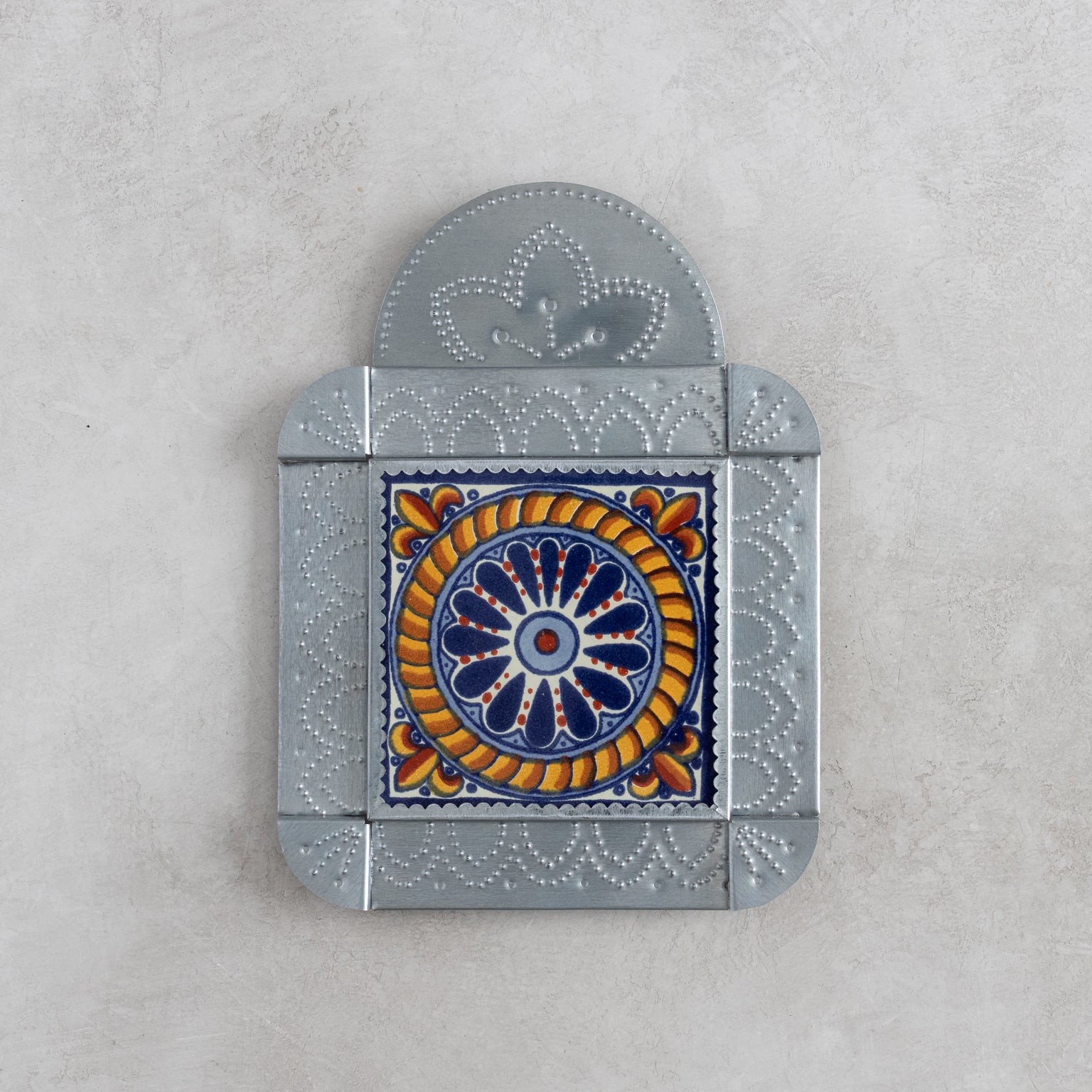 Decorative wall decor tile in tinwork frame with a central floral design on a gray background
