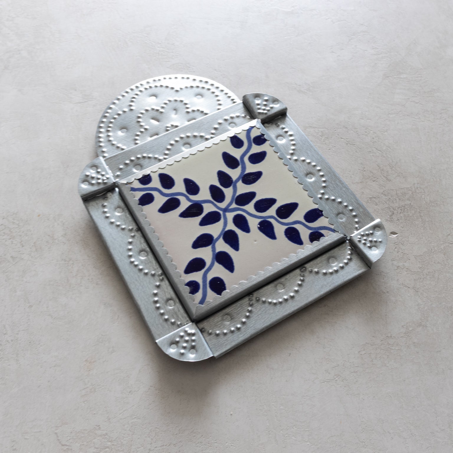 Decorative tinwork framed tile with blue vine pattern on a light gray background
