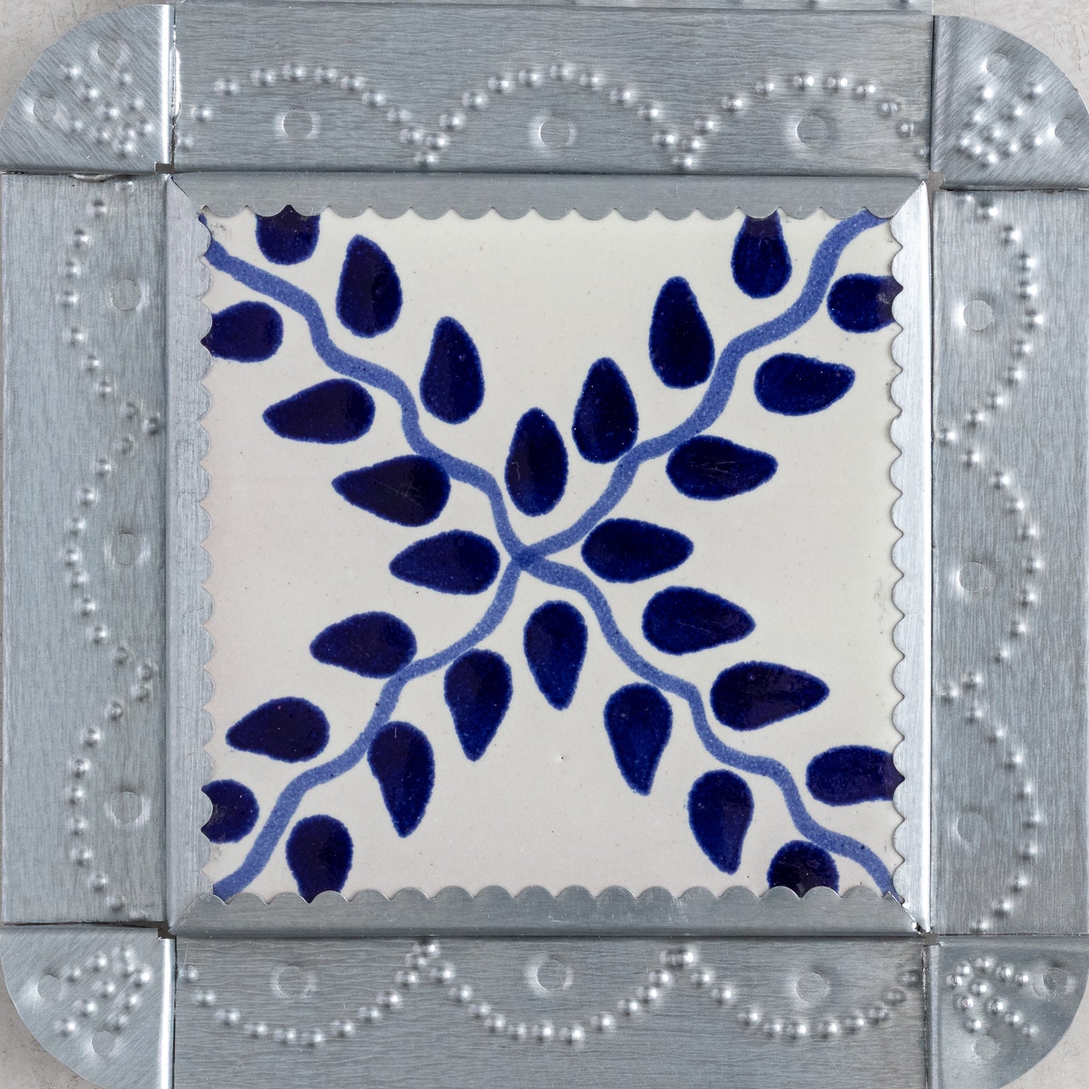 Closeup of a decorative tinwork framed tile with blue vine pattern on a white background