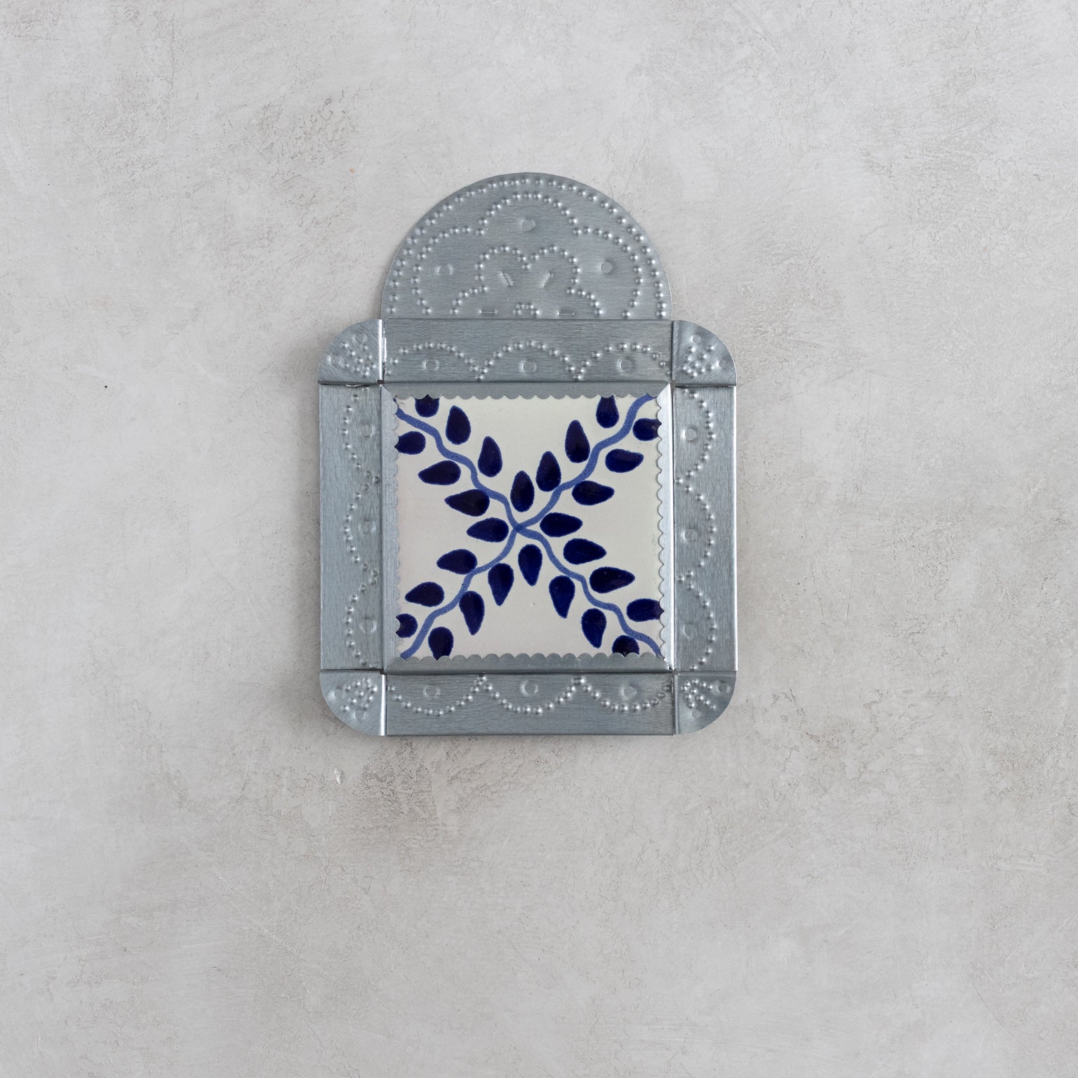 Decorative tinwork framed wall tile with blue leaf design on a gray background