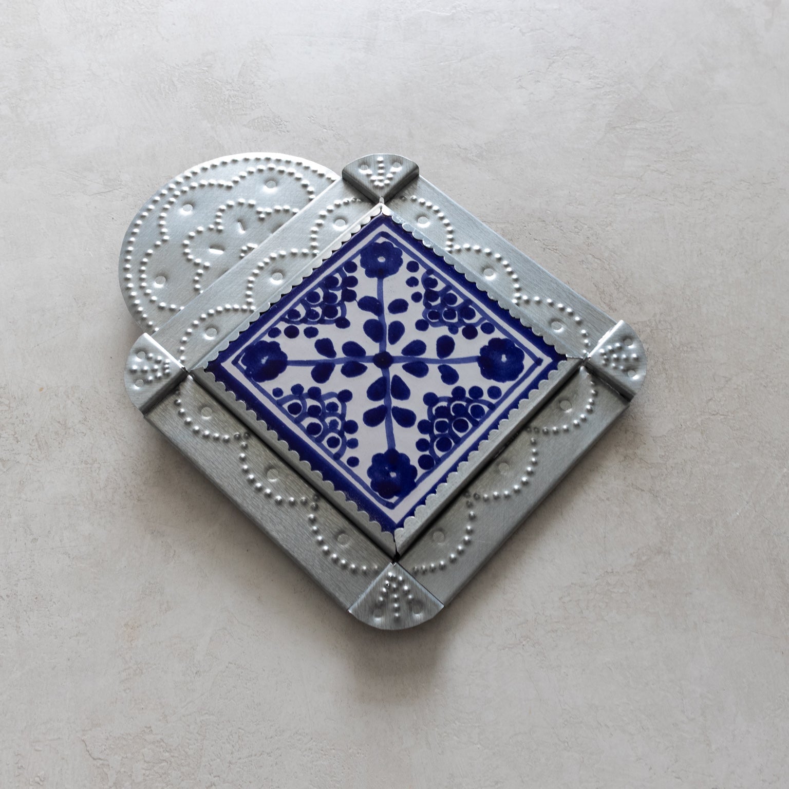 Decorative tinwork framed tile with blue floral pattern on a light gray background