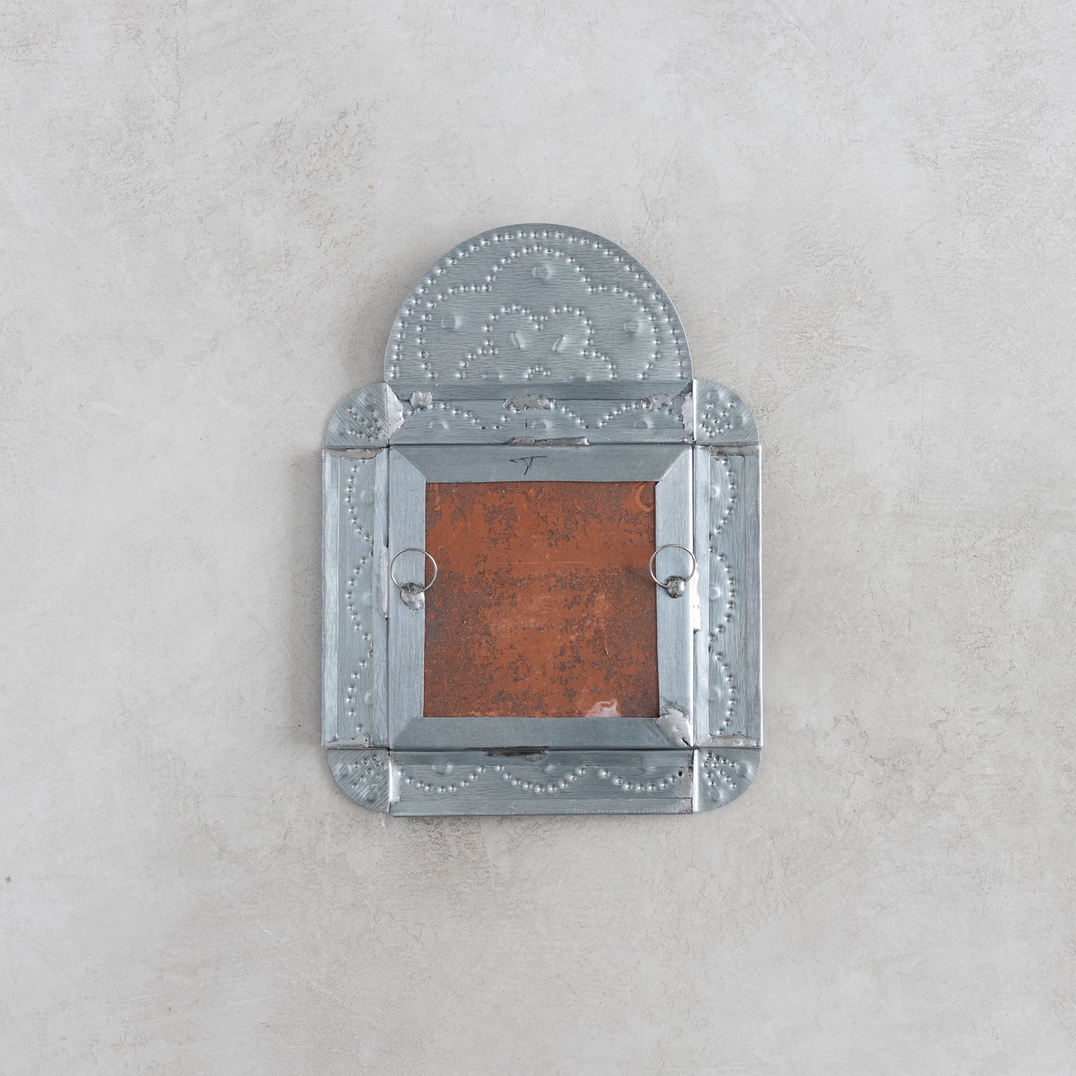 Back of a decorative tinwork framed tile on a light gray background