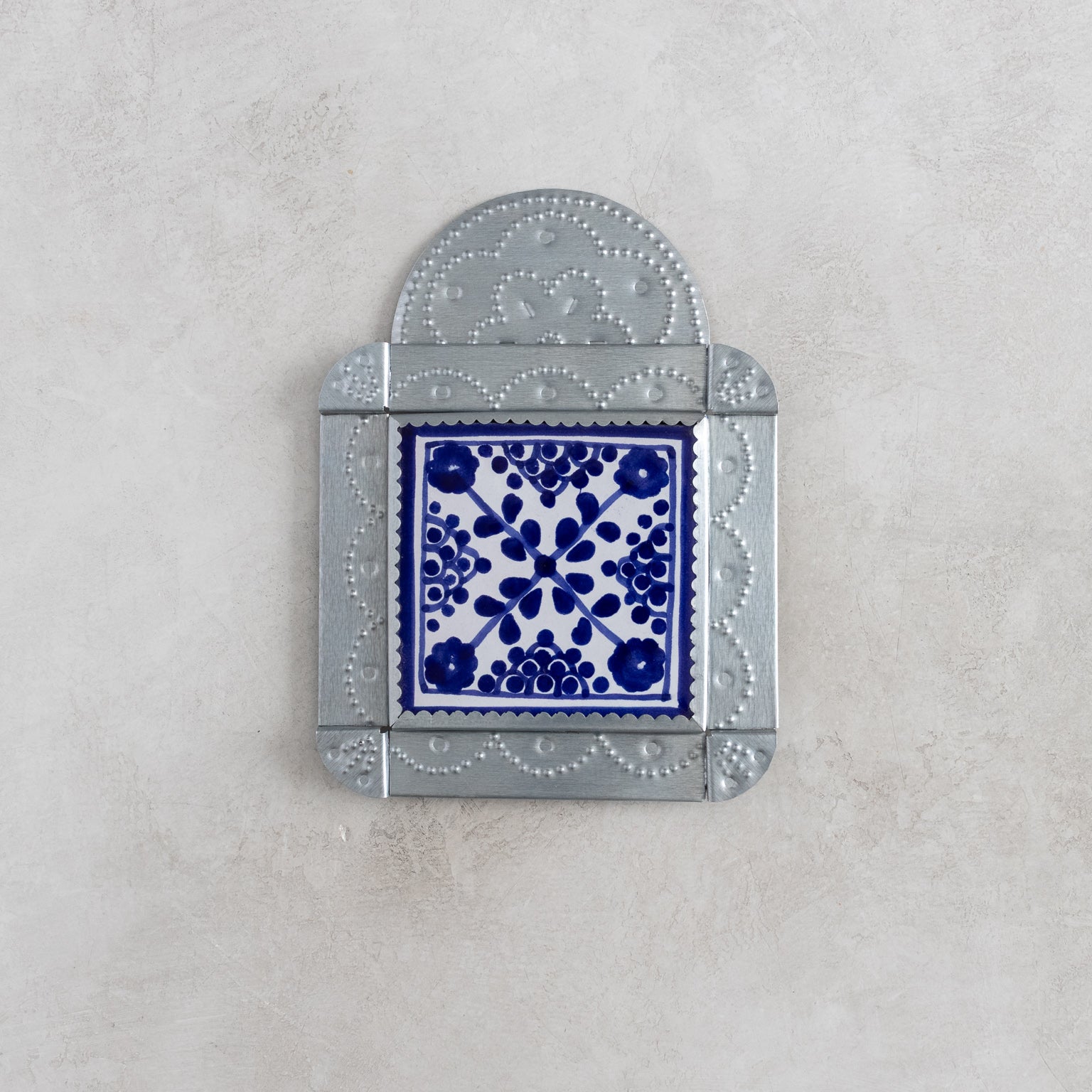 Decorative tinwork framed wall tile with blue floral pattern on a gray background