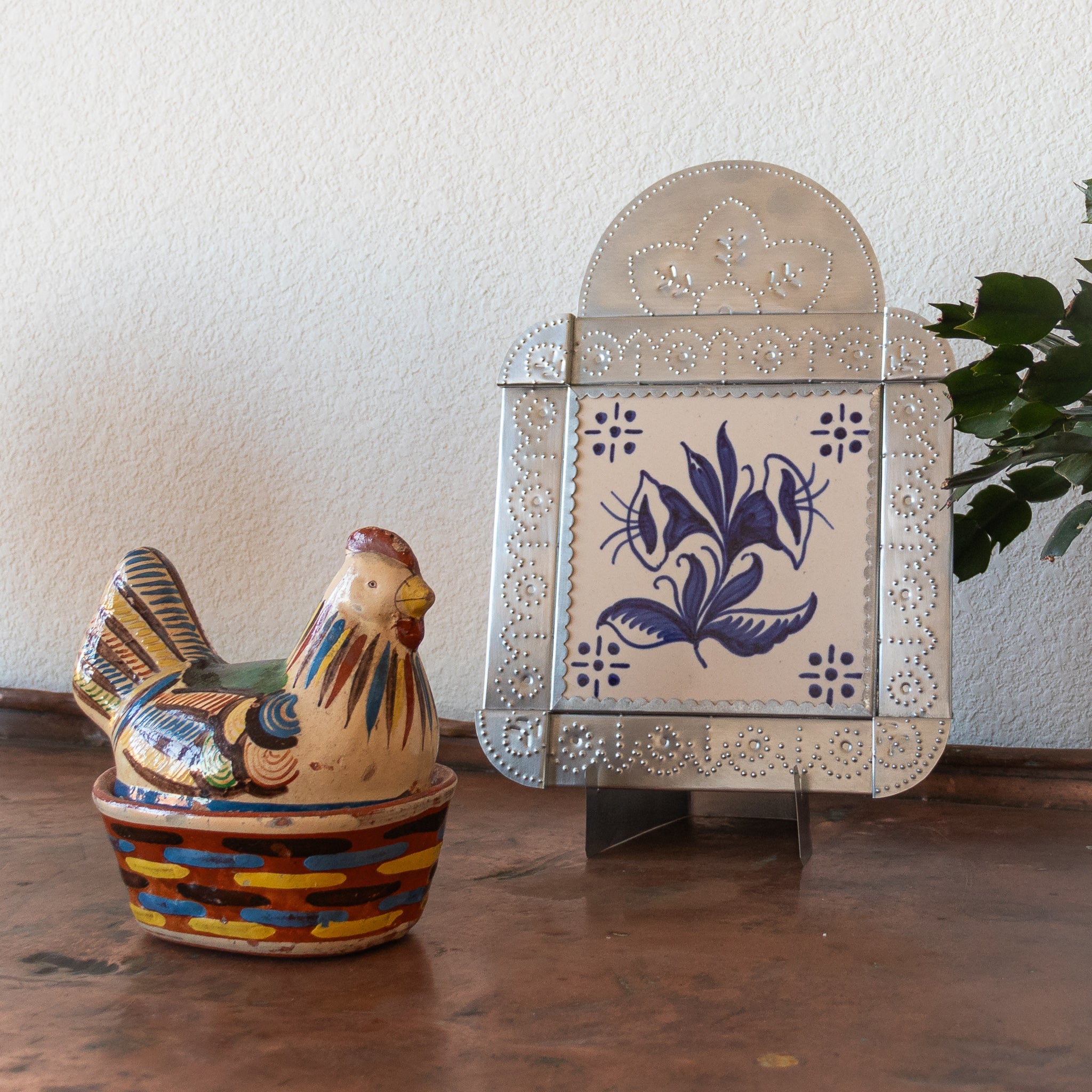 Decorative tinwork framed tile with a Calla Lilly on a table with a ceramic chicken