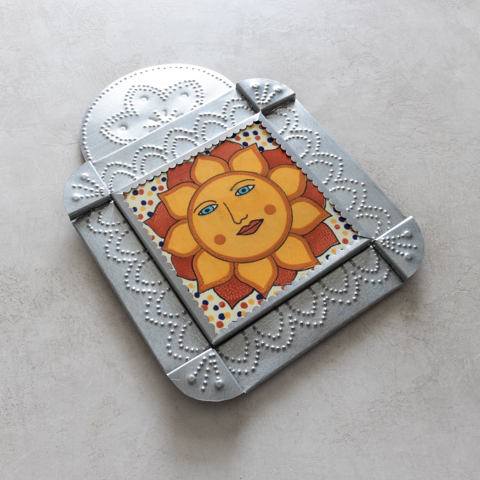 Decorative tinwork framed tile with a sun design on a light gray background