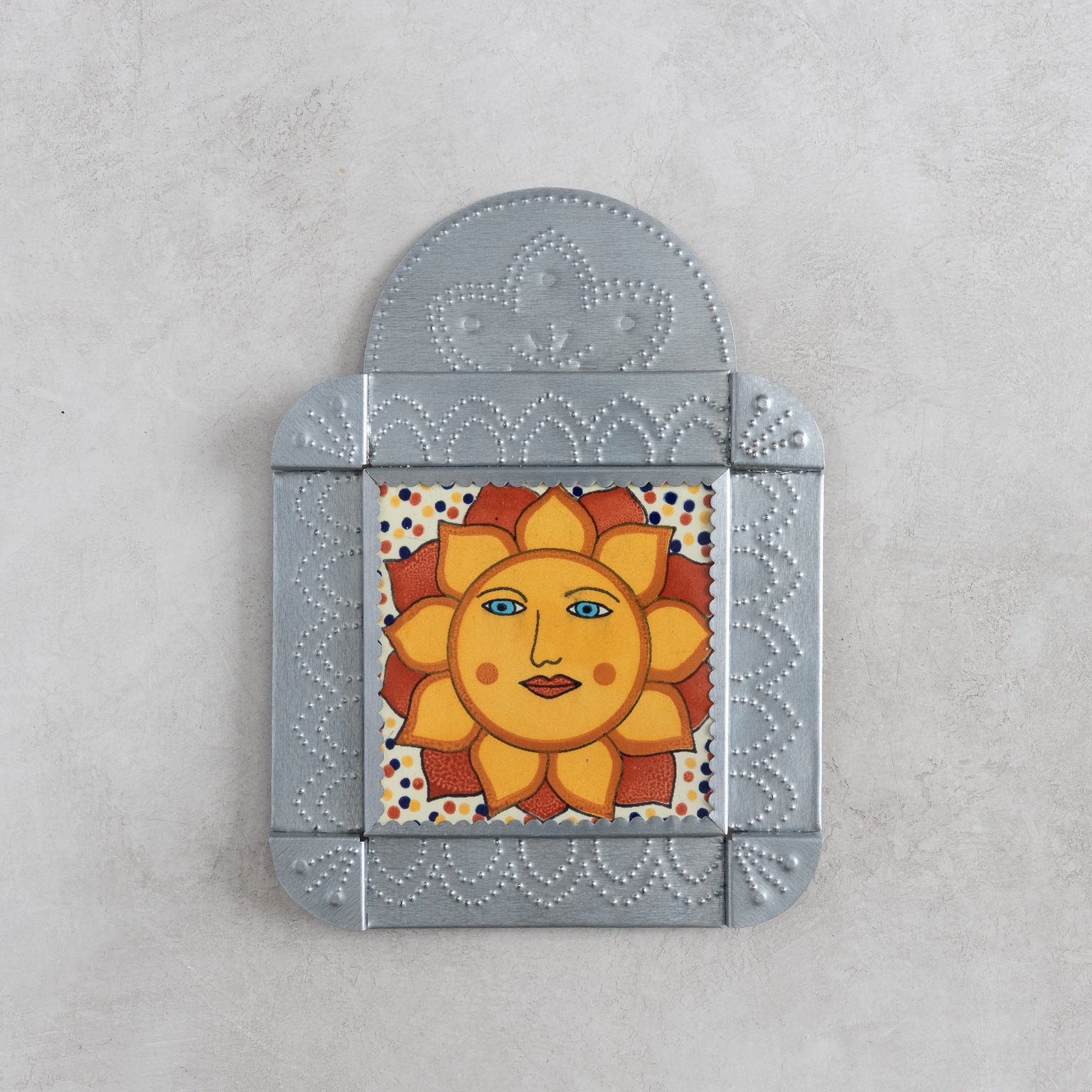 Decorative talavera tile with a sun design in a tinwork frame on a light gray background