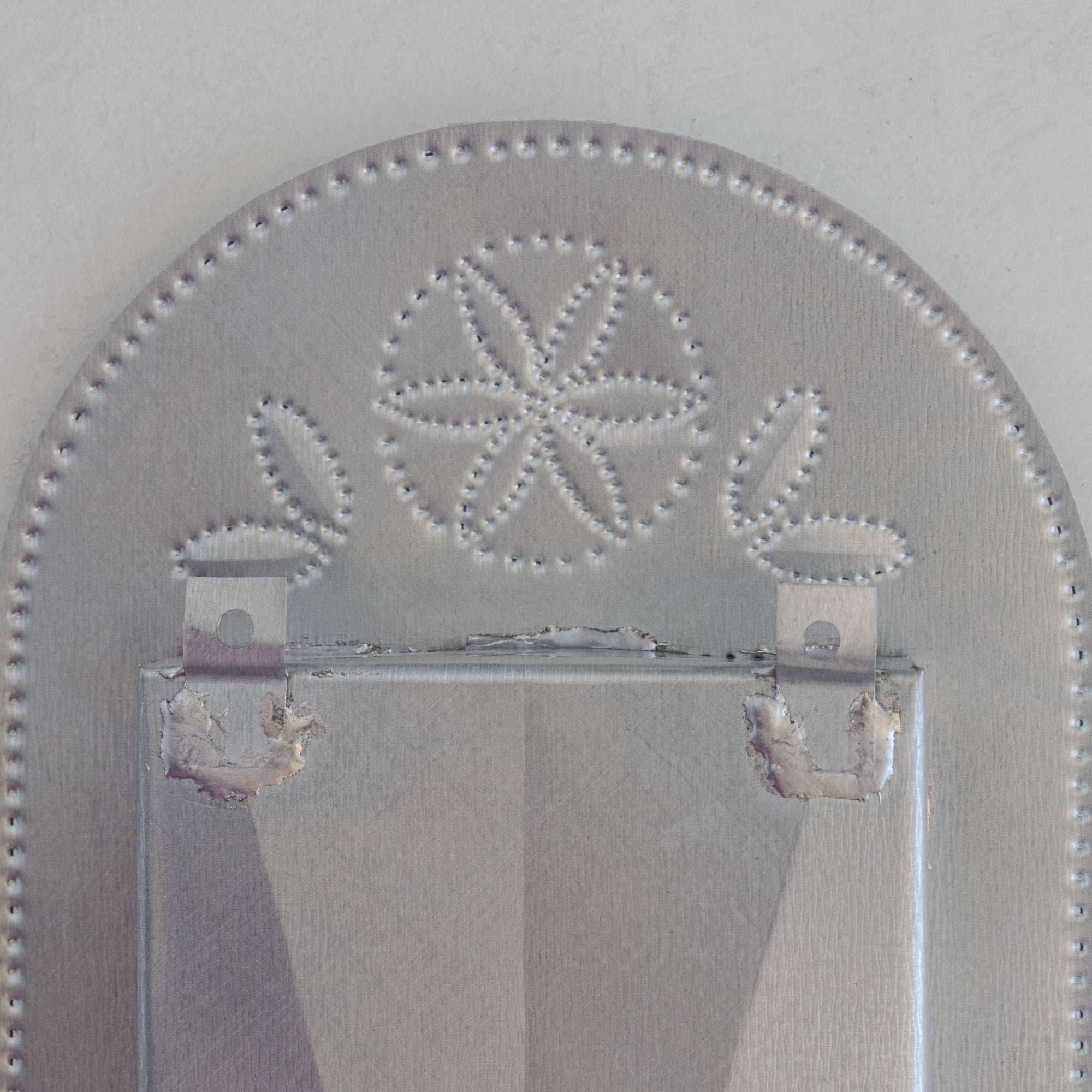 Back of Nicho de Recuerdo showing hand-punched floral motif visible through the tin, two hanging tabs, and soldered box construction.